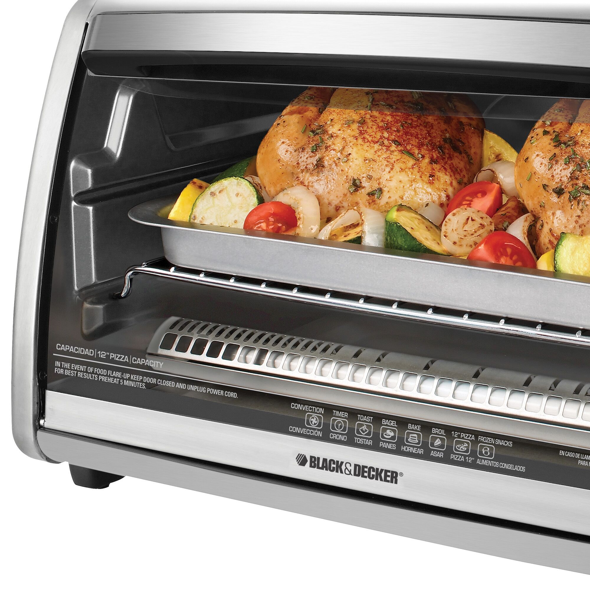 Close up of countertop convection toaster oven with roasted vegetables and chicken.