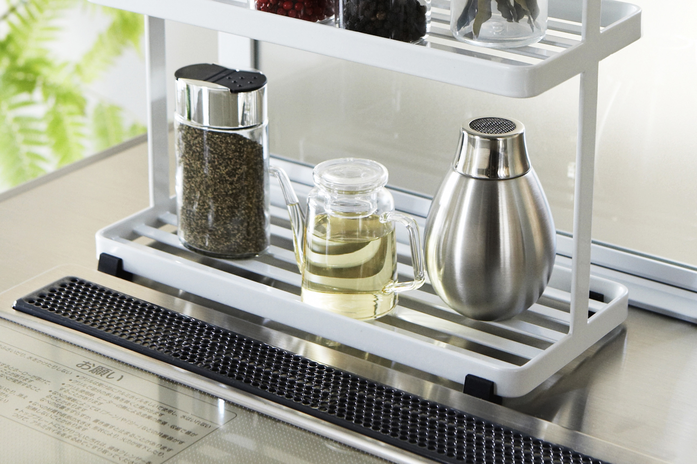Zoomed in photo of Two tiered white rack with slatted shelves filled with spices on kitchen countertop.