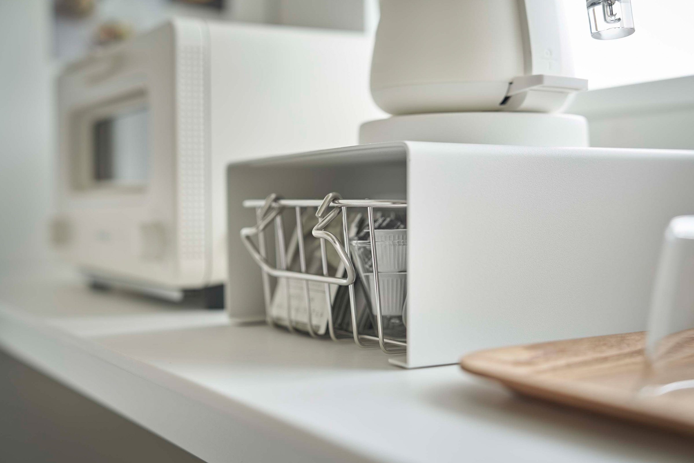 Close up of white Yamazaki Home Stackable Countertop Shelf with a basket of tea underneath