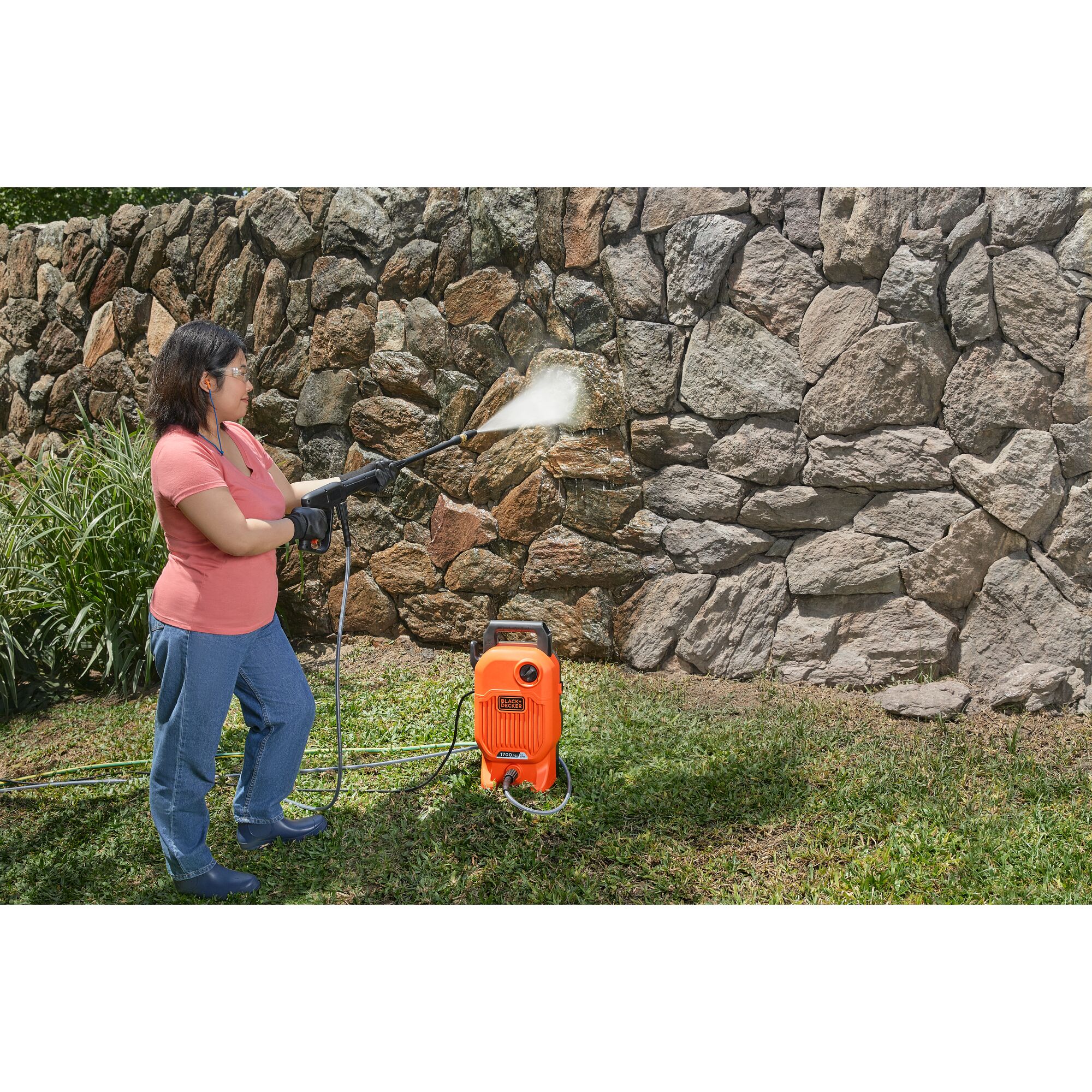 Woman using BLACK+DECKER 1,700 MAX psi* pressure washer with the turbo nozzle to clean a dirty stone wall