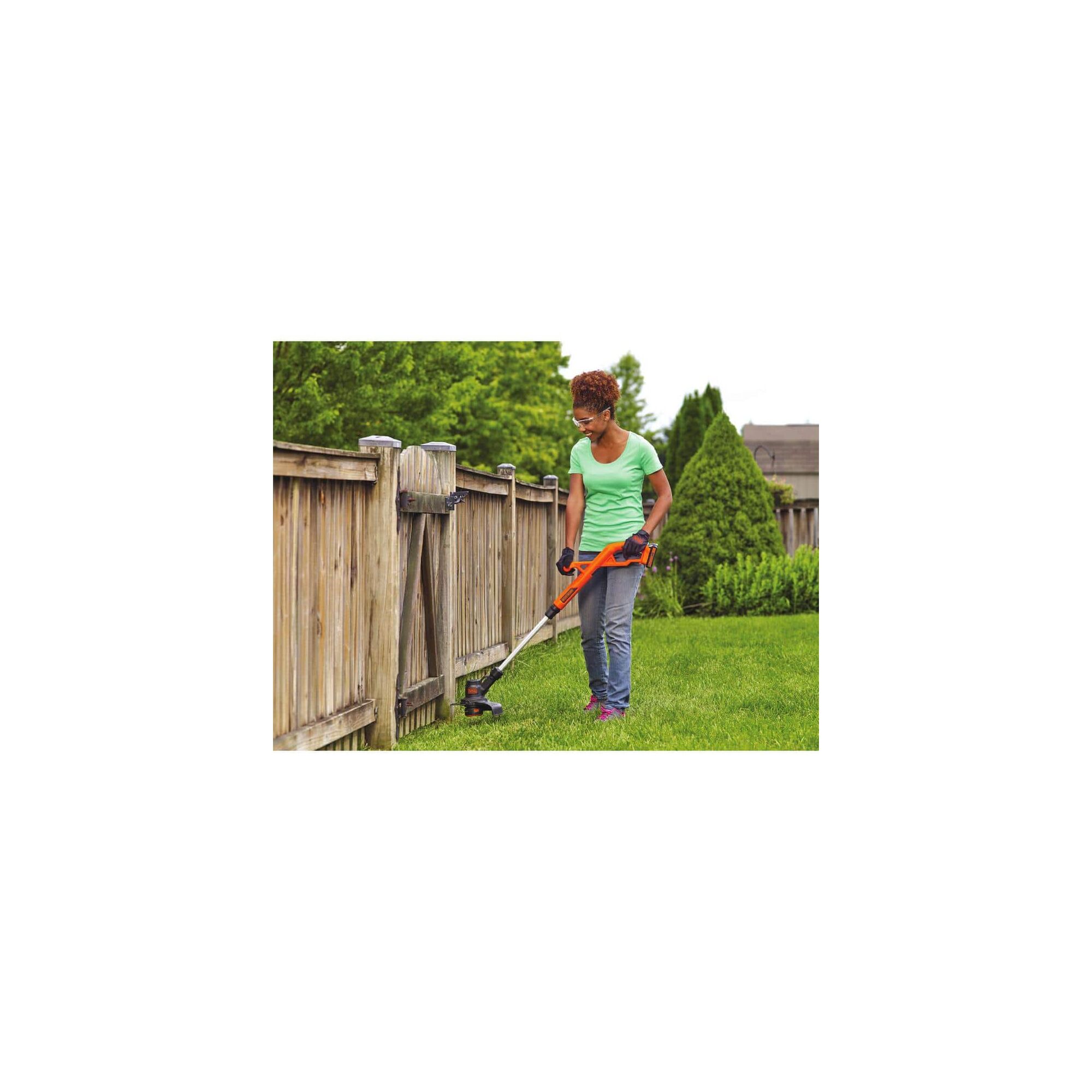 Woman using string trimmer near a wooden fence