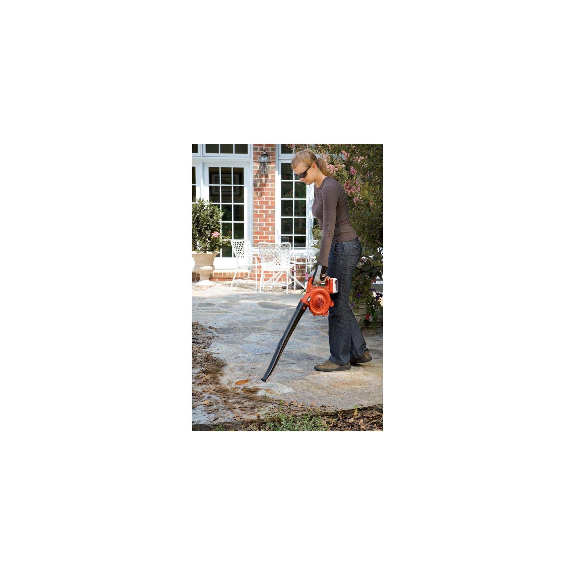 Woman using 40V Max Lithium Sweeper to blow leaves off of a stone walkway.