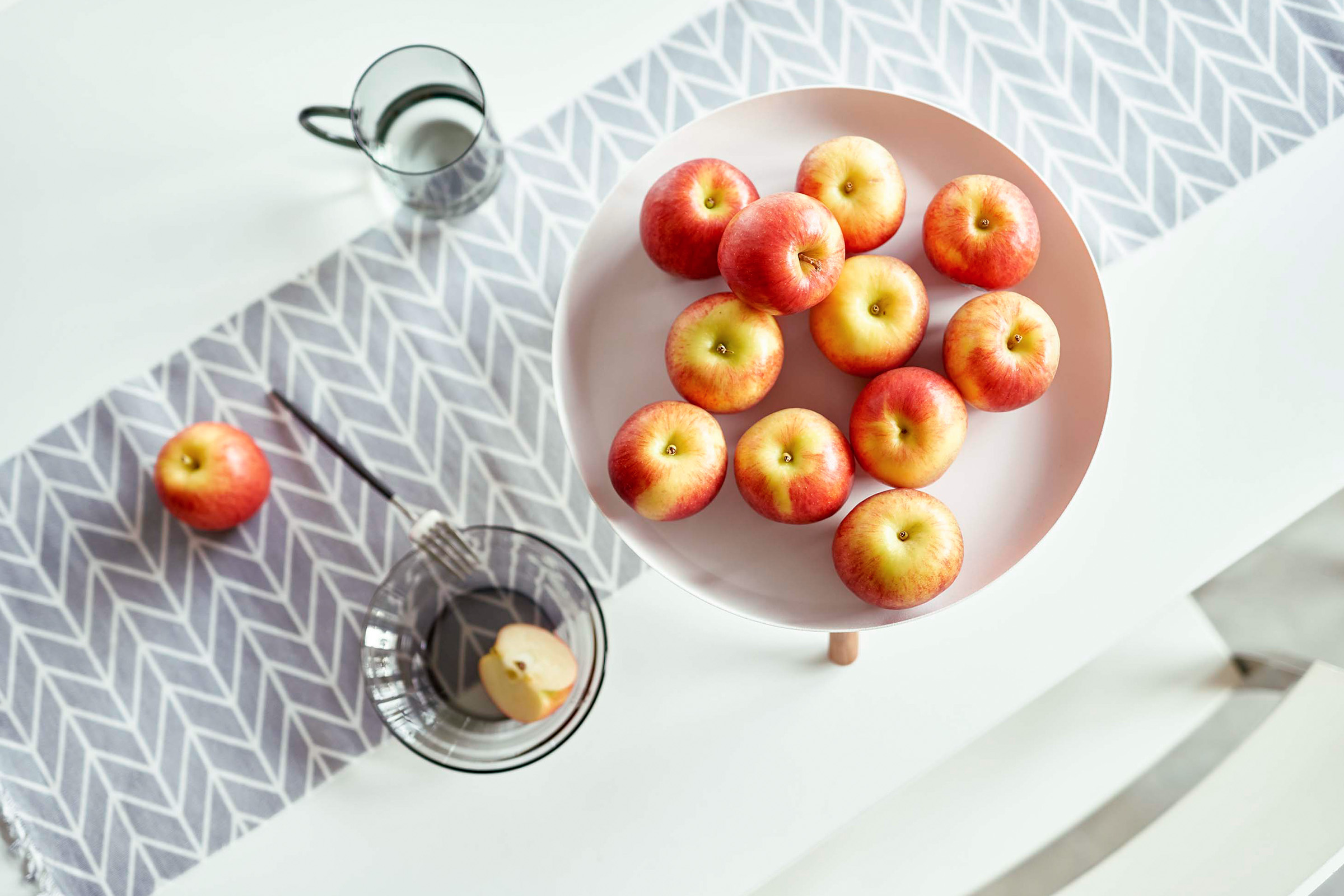 Aerial view of a white round steel pedestal stand on top of a dinner table. The stand is holding apples.