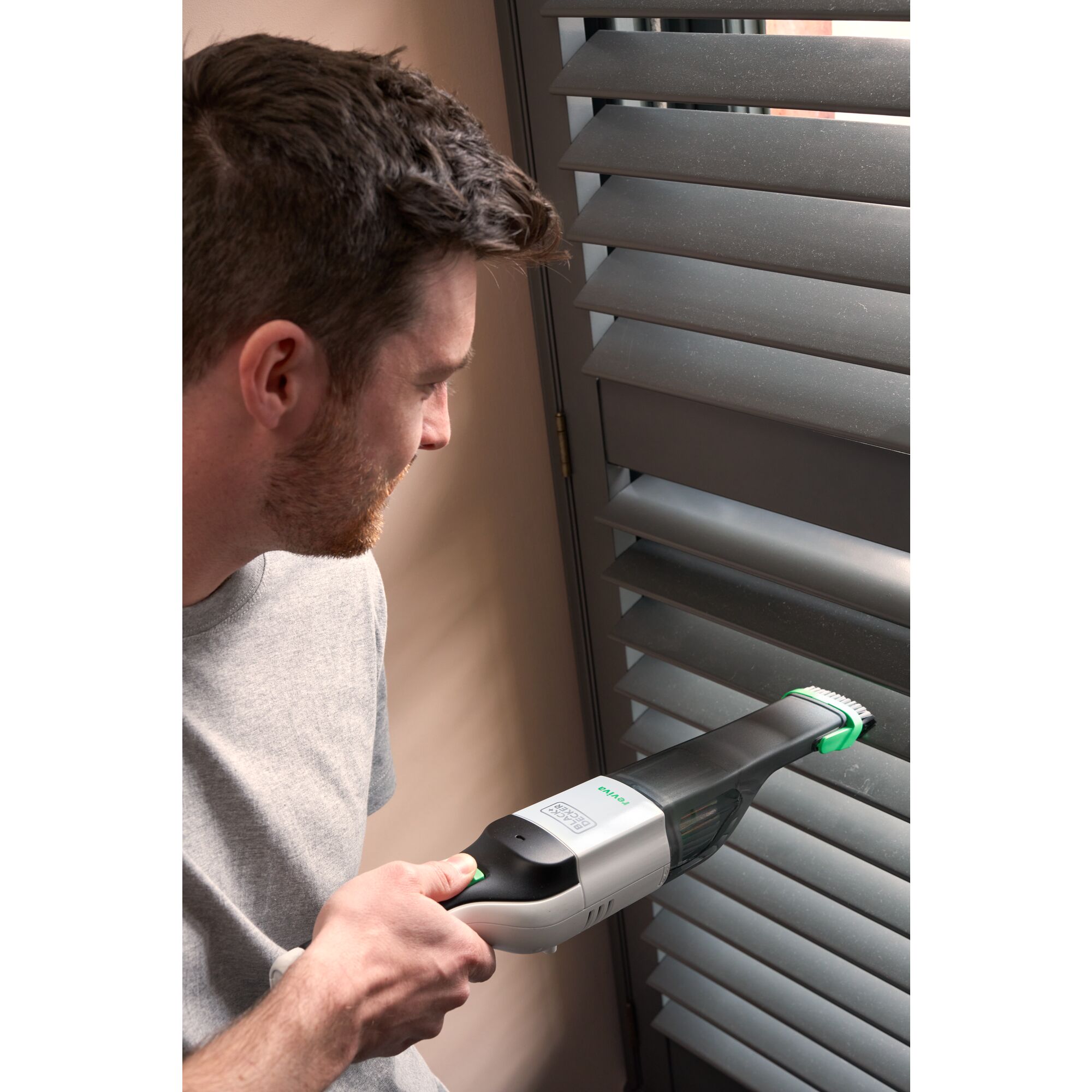 Man cleaning blinds with 8V MAX* reviva™ Hand Vac.