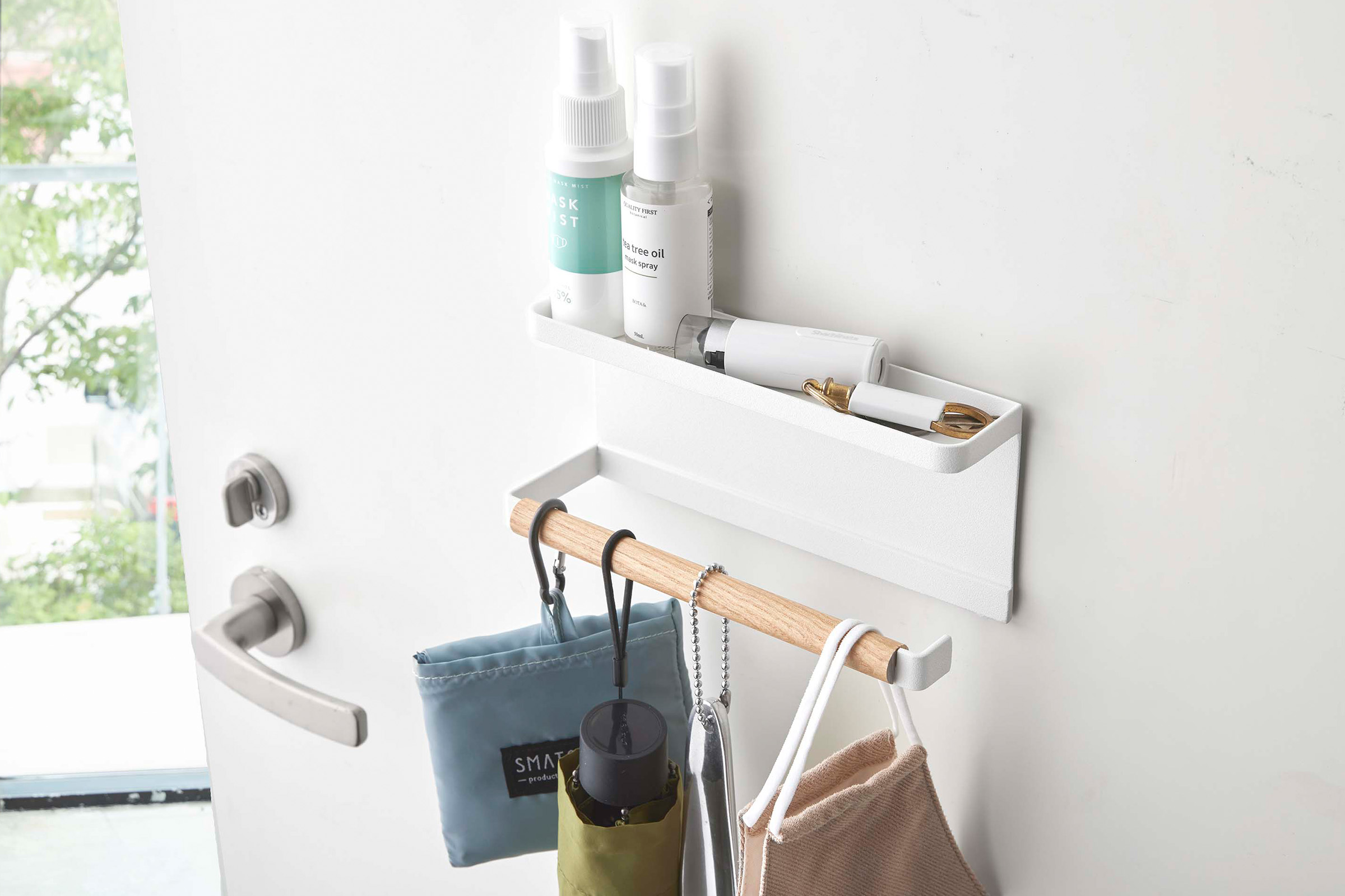 Magnetic Umbrella Holder by Yamazaki Home mounted on a door holding masks, hand sanitizer sprays, and other entryway items.