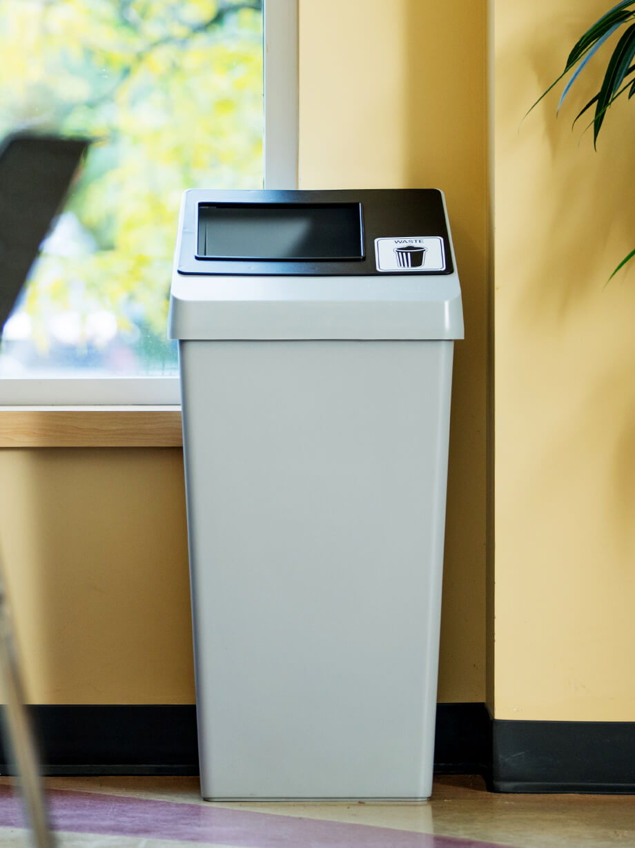 durable plastic waste bin with sloped lid and restrictive black opening in a college cafeteria