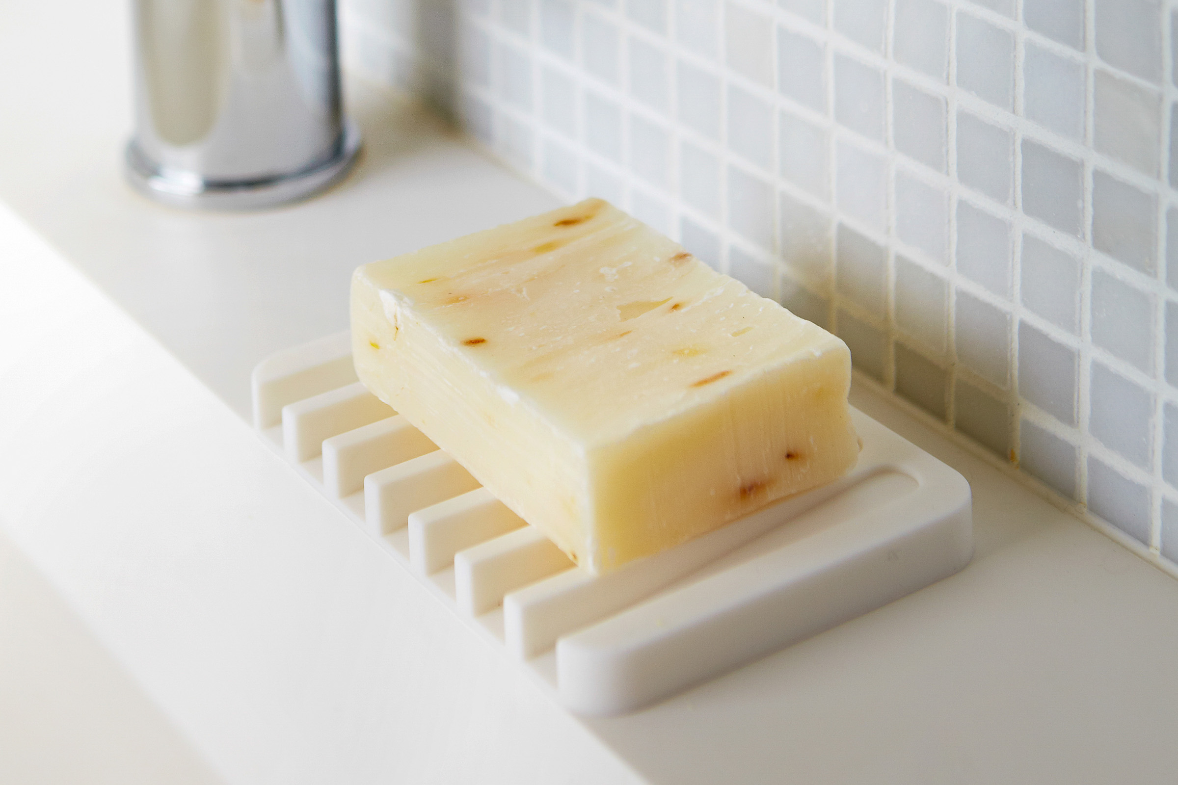 White Self-Draining Soap Tray holding soap bar on bathroom sink countertop by Yamazaki Home.