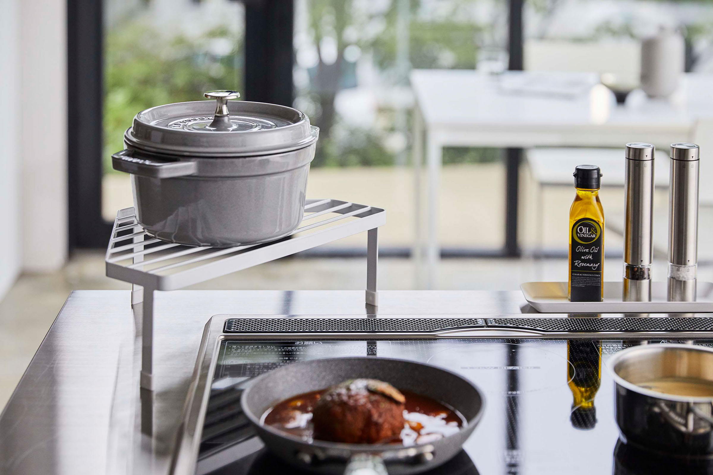 Front view of White Corner Riser holding pot next to kitchen stovetop by Yamazaki Home.