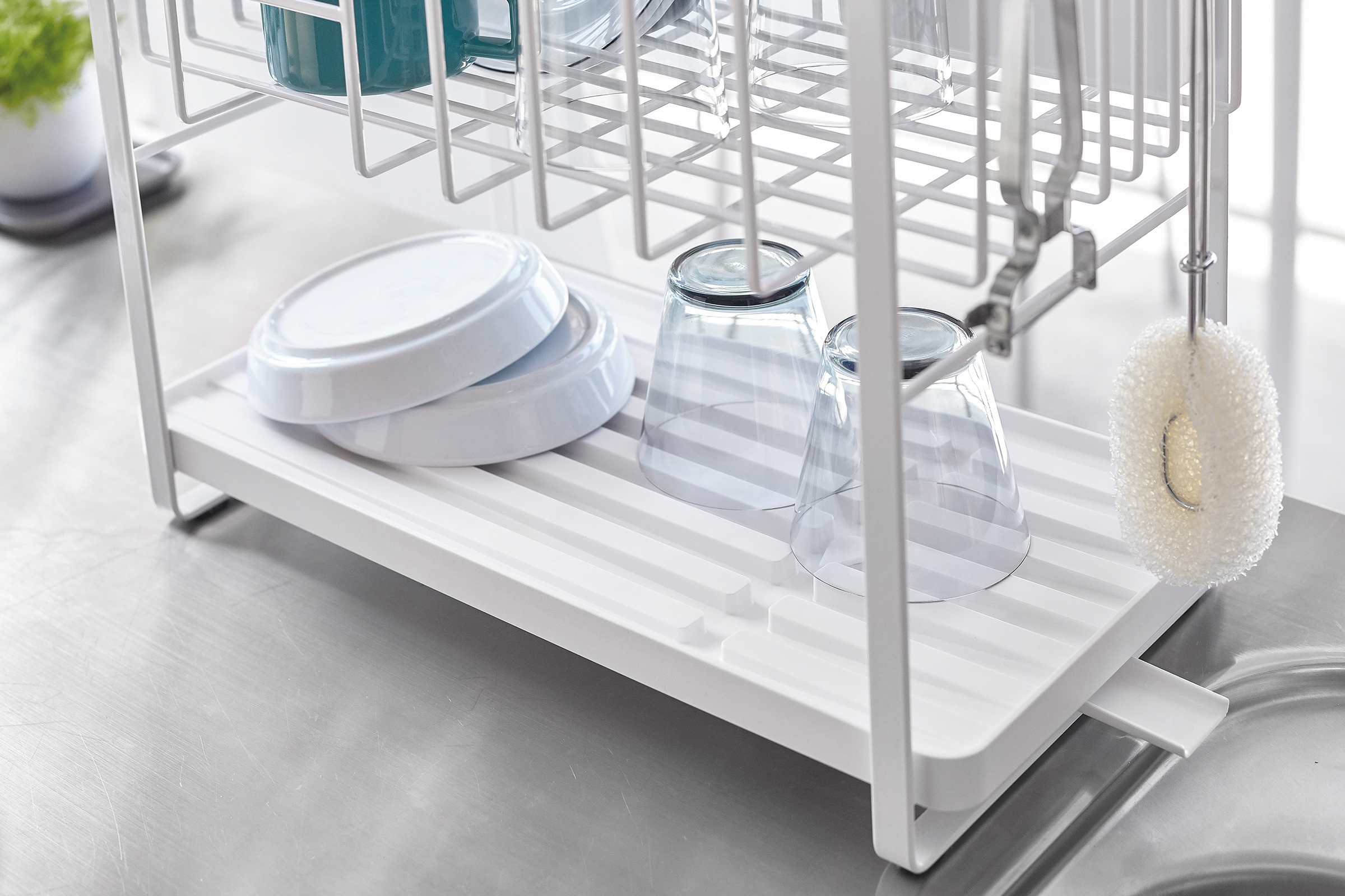 White Two-Tier Customizable Dish Rack holding bowls and cups on kitchen sink countertop by Yamazaki Home.

