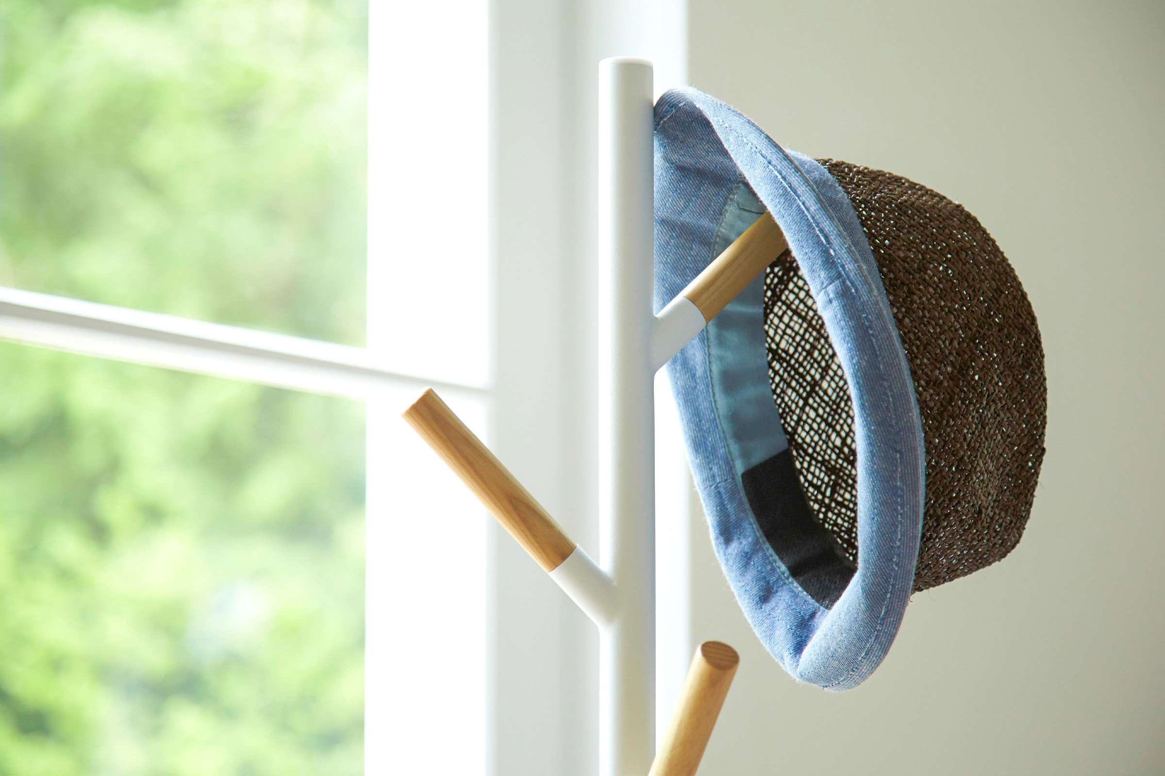 Close up view of white coat rack holding hat by Yamazaki Home.