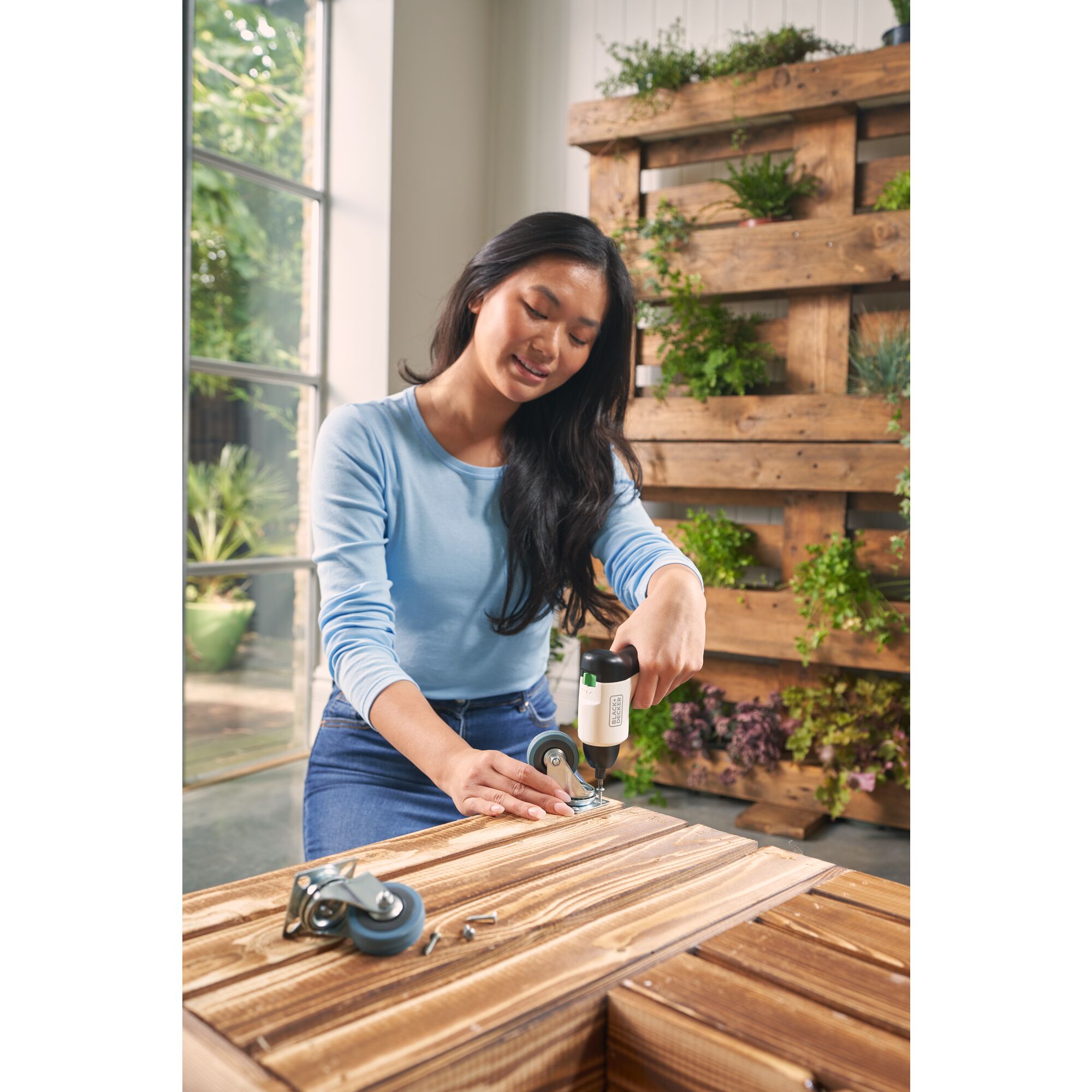 Woman using reviva™ 4V MAX* Screwdriver to attach casters to bottom of a wood crate.
