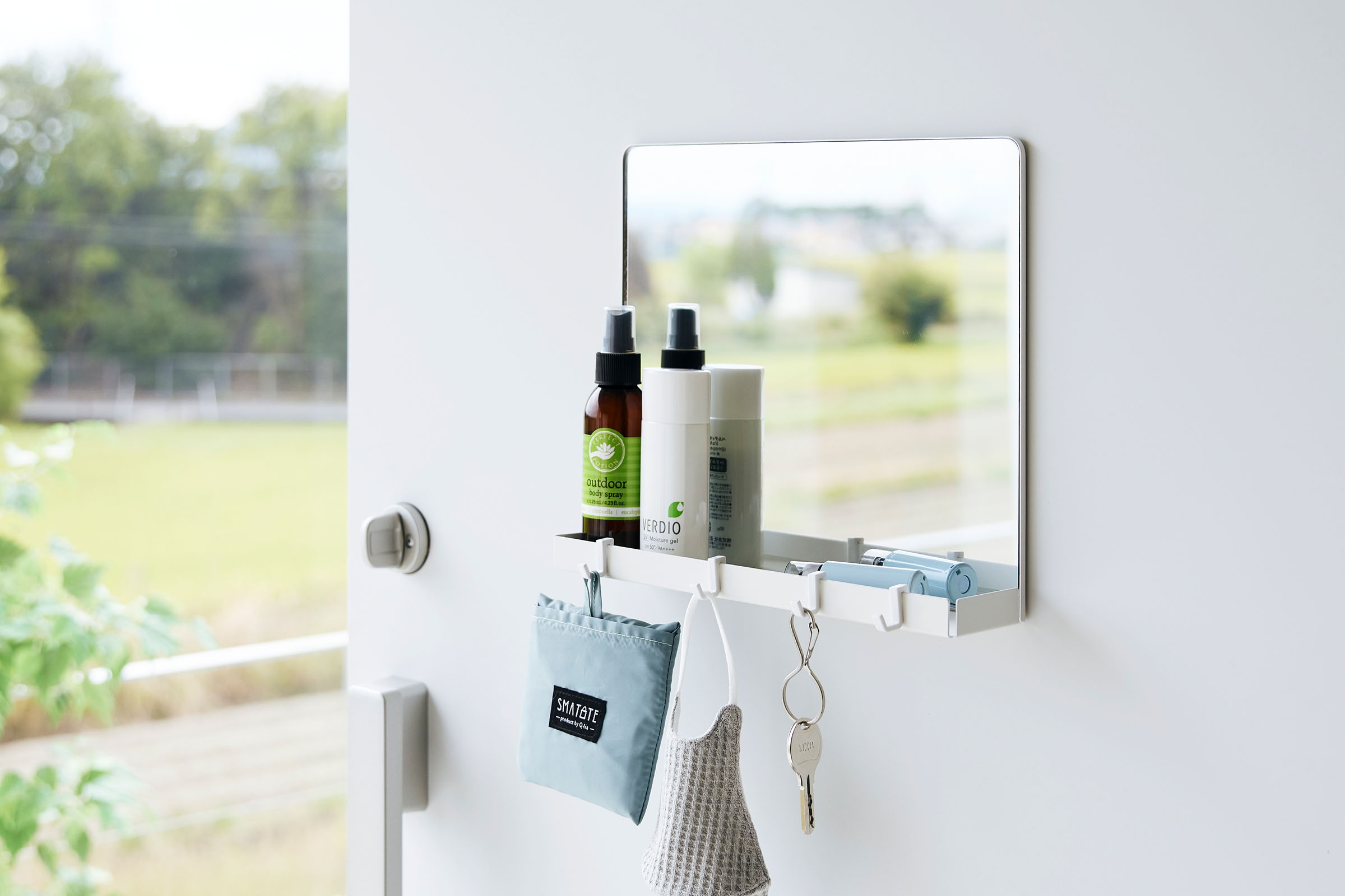 A close up of a white Yamazaki Magnetic Mirror With Storage Rack attached to a door withholding bottles.