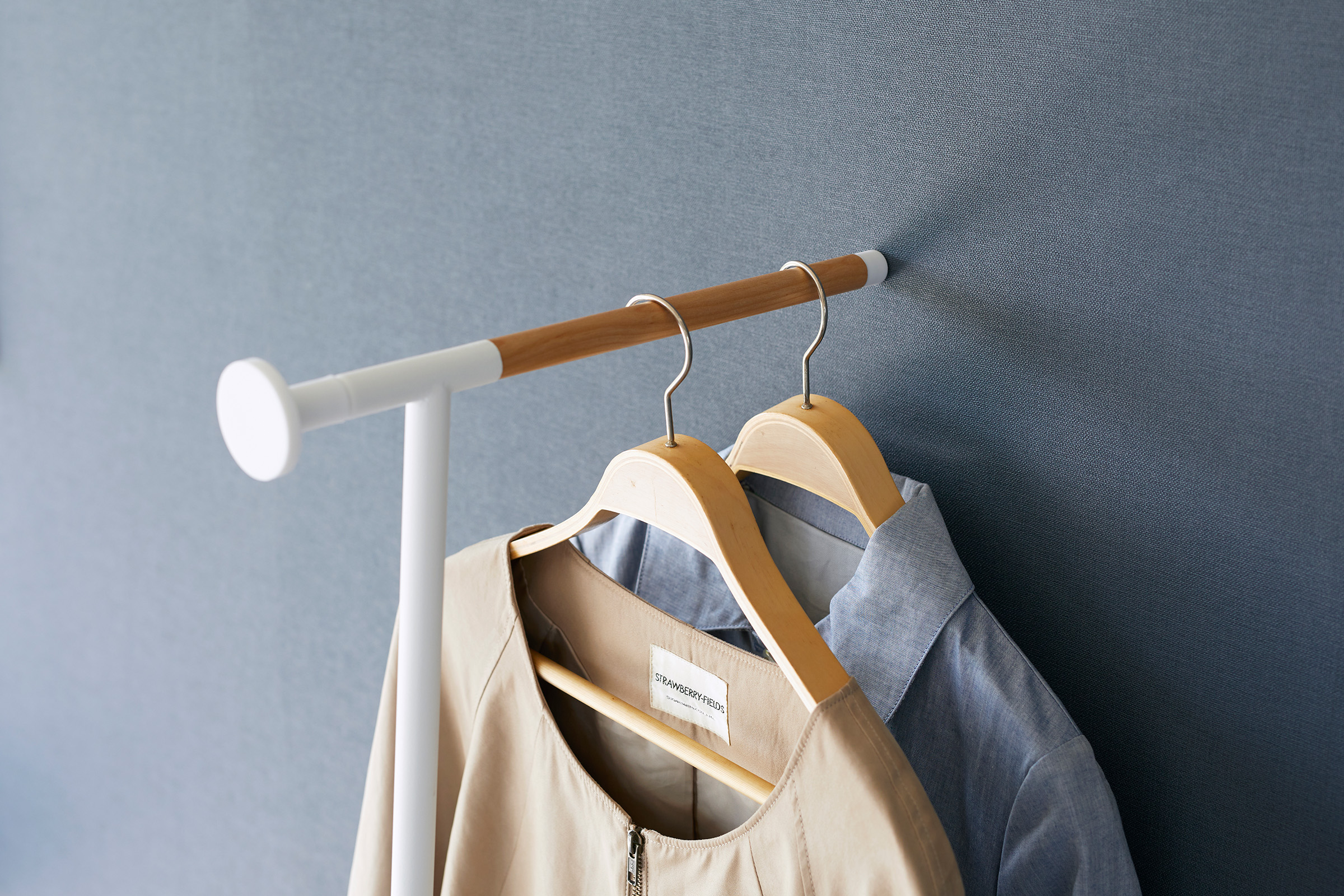 The top part of the Clothes Steaming Leaning Pole Hanger by Yamazaki Home in white leaning on a wall holding two hangers with clothes.
