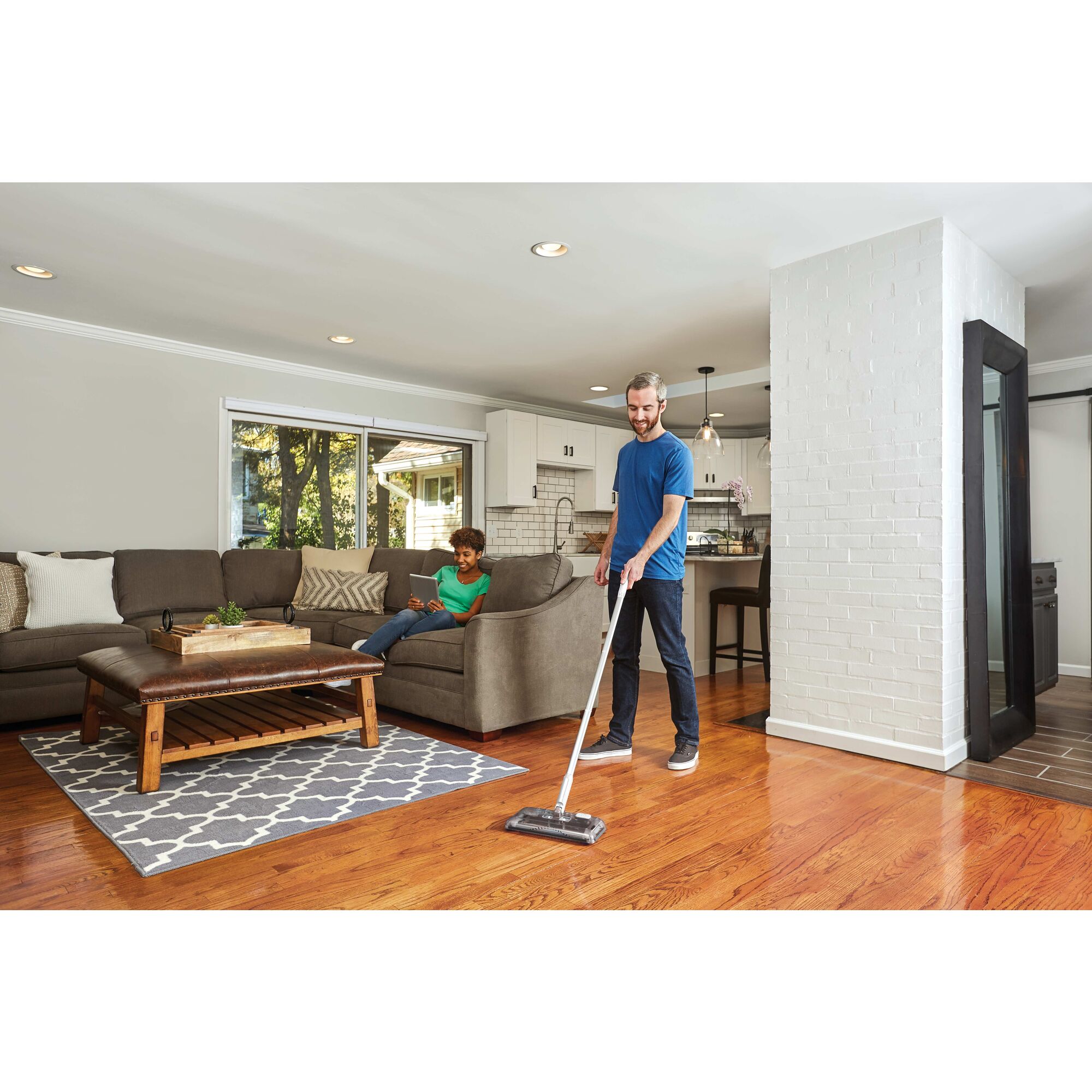 Person cleaning the living room floor with BLACK+DECKER floor sweeper