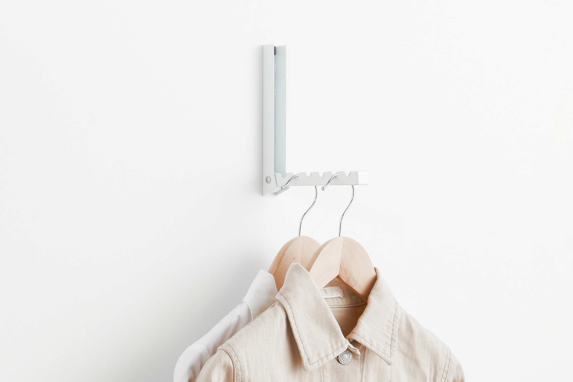 Over-the-Door Hook by Yamazaki Home in white on a wall, holding two hangers with clothing items.