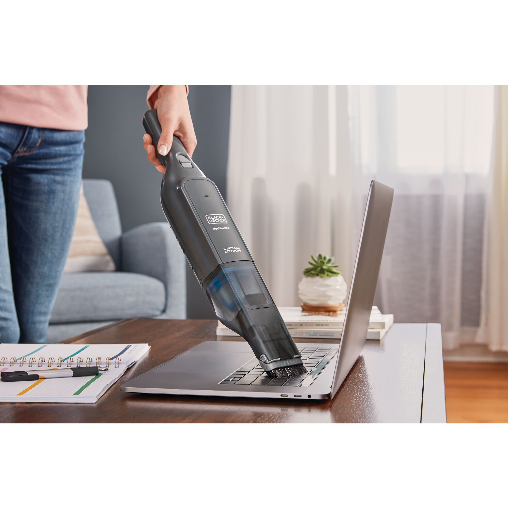 Person cleaning laptop with BLACK+DECKER Dustbuster
