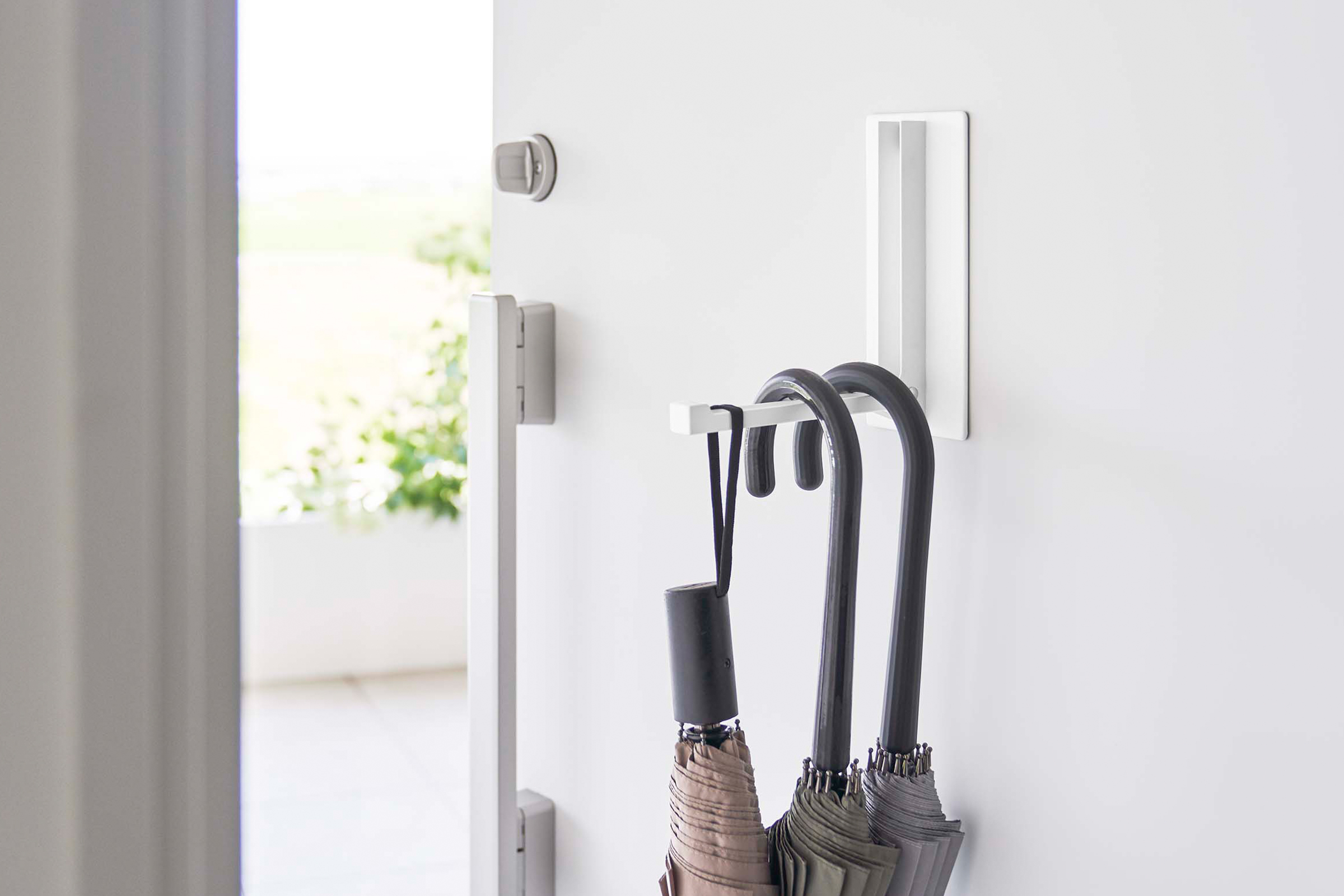 A sleek white metal hook, seamlessly mounted on the back of a door, boasts a retractable design that can conveniently accommodate three umbrellas, maximizing space utilization.