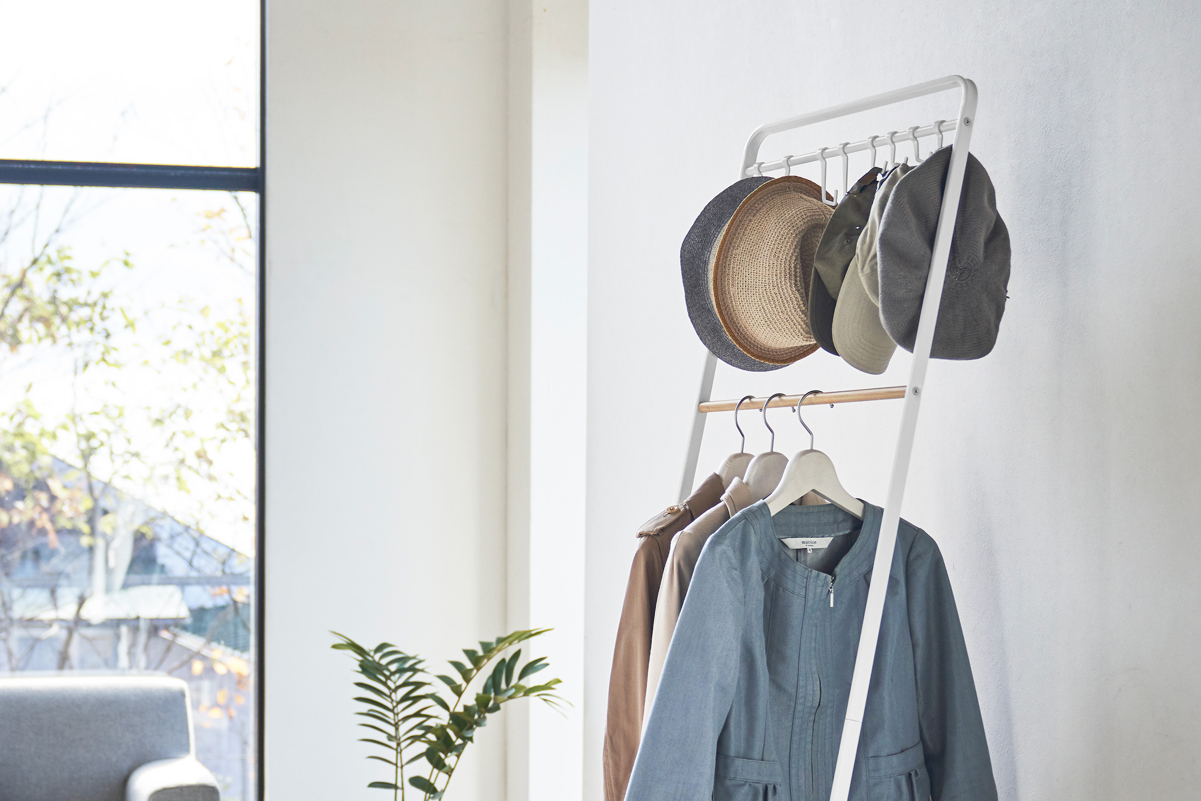 The top half of Coat Rack with Hat Storage by Yamazaki Home in white holding a number of tops on the bottom rack and hats on the hooks above.