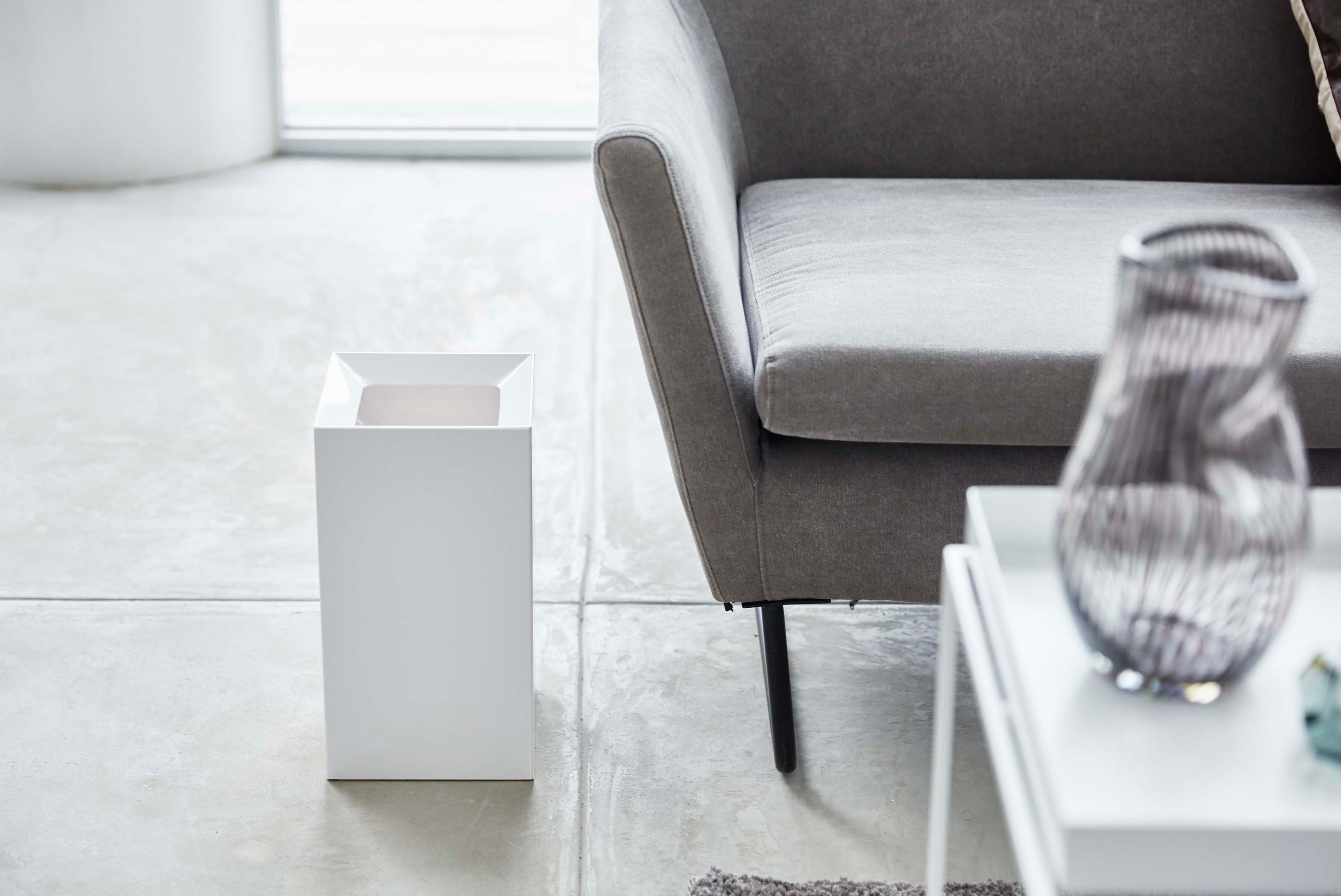 Front view of square white trash can in living room by Yamazaki Home.