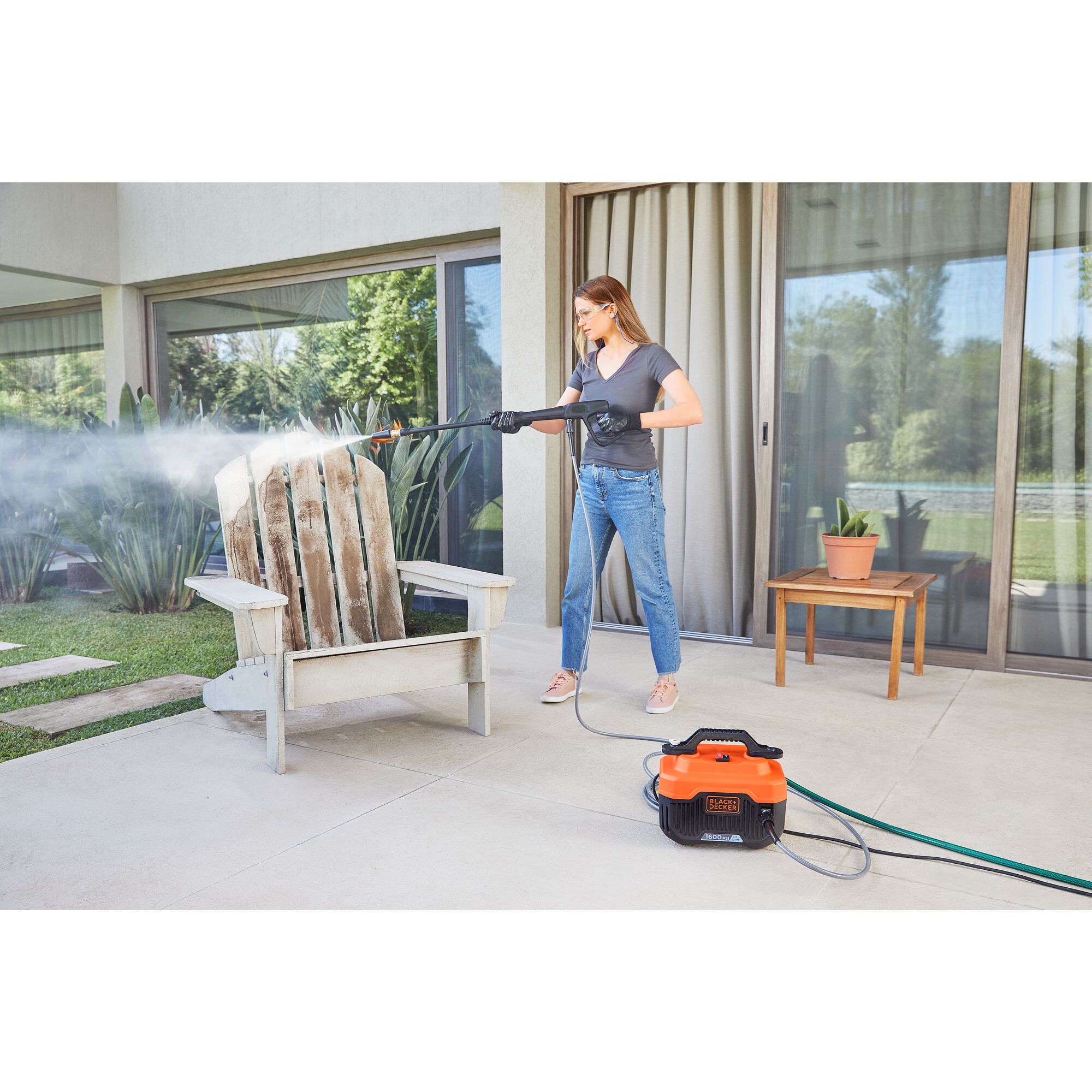 Woman using BLACK+DECKER 1,600 MAX psi* pressure washer with turbo nozzle to clean patio chair on a patio outside a house