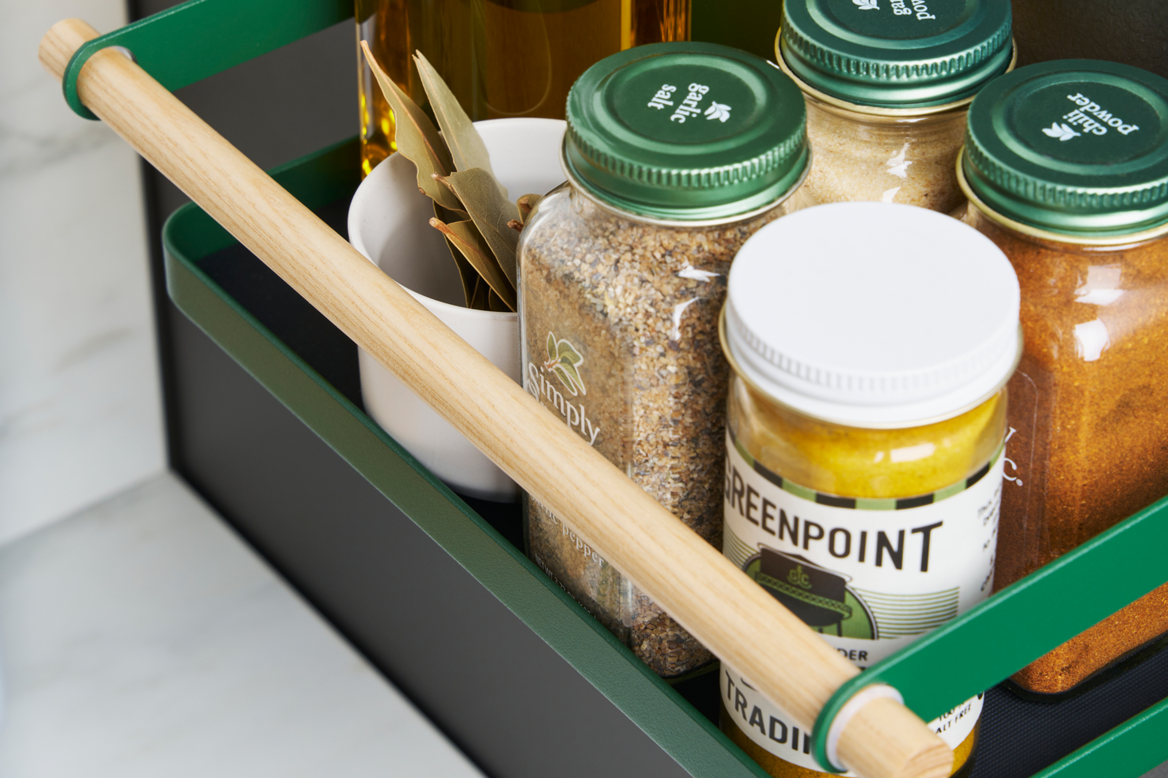 Close up top-down view of Forest Green Yamazaki Home Magnetic Storage Caddy with oil, herbs and spices stored attached to a refrigerator.