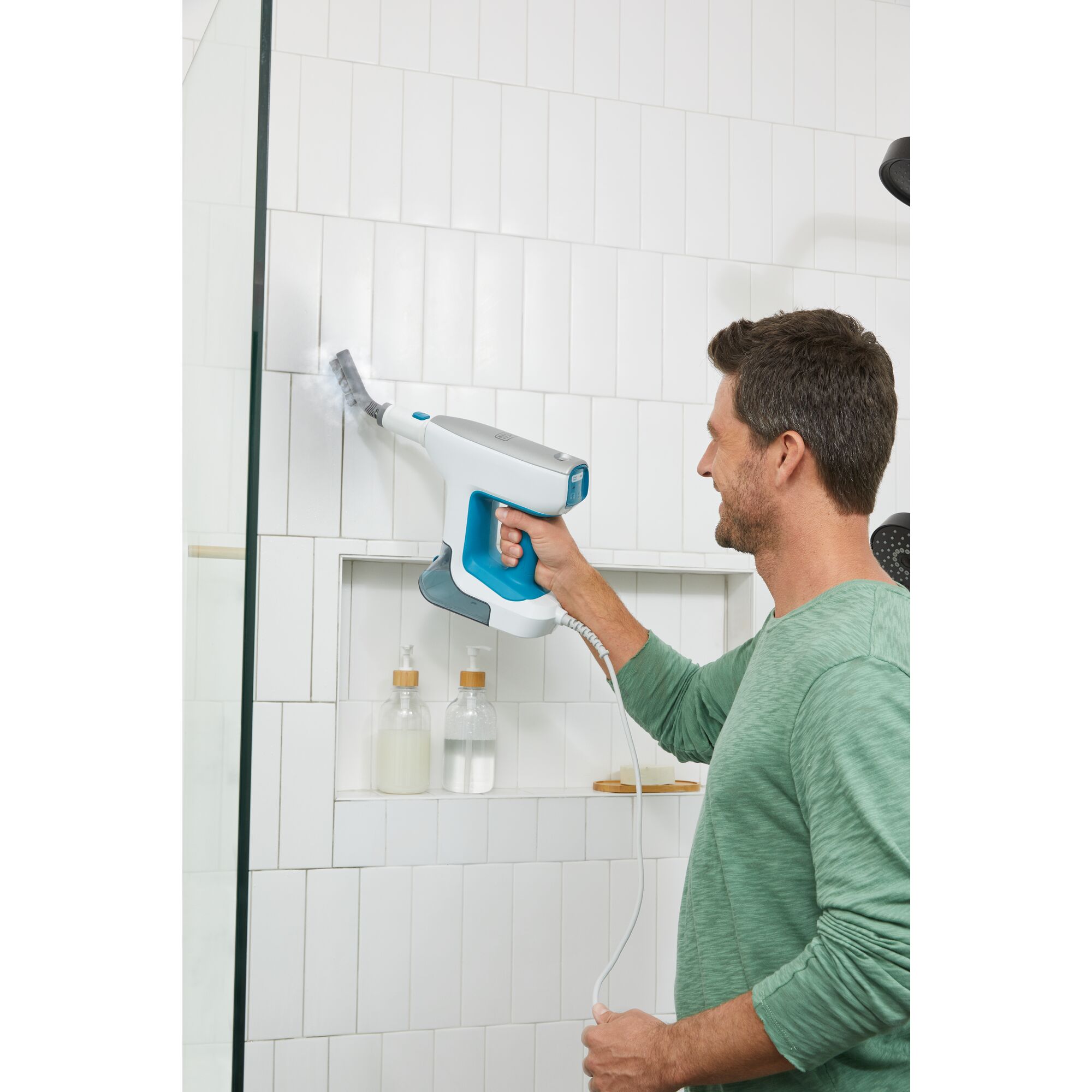 Man using steam mop accessory to clean shower tile in a stand up shower