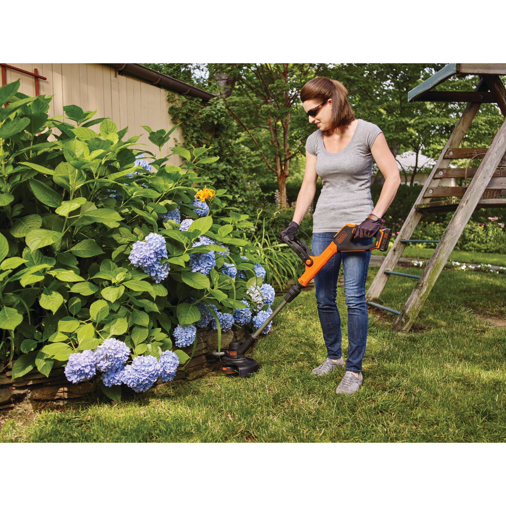 Woman using 20V Max Lithium Easyfeed string Trimmer/Edger near garden and playset.