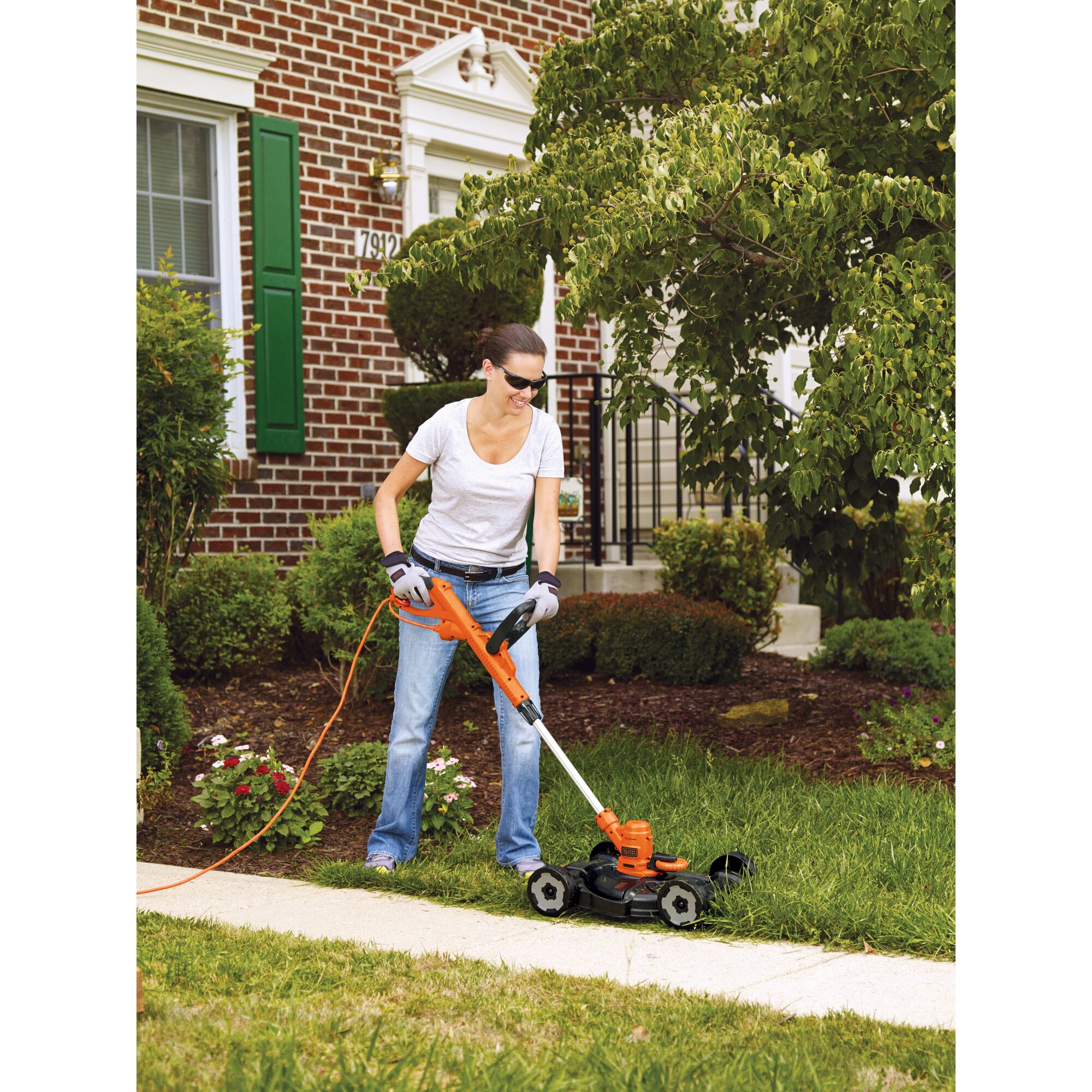 Woman using 3-In-1 String Trimmer/Edger & Lawn Mower along edge of a sidewalk.