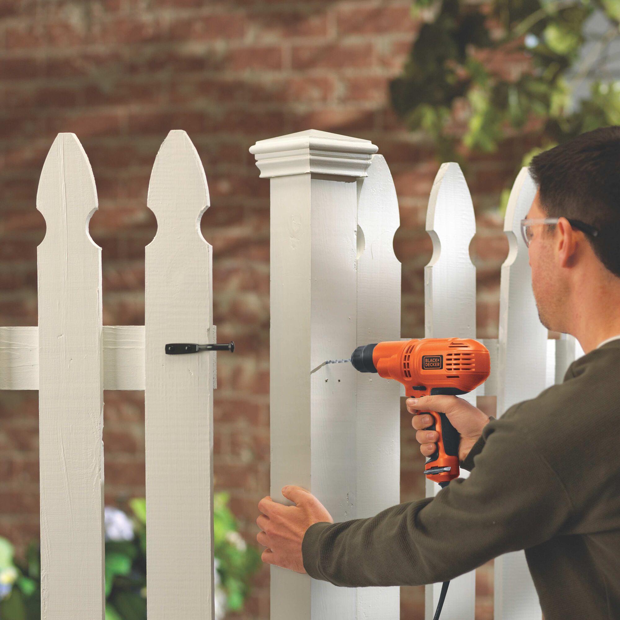 Man using BLACK+DECKER 5.5am Electric drill on a white picket fence