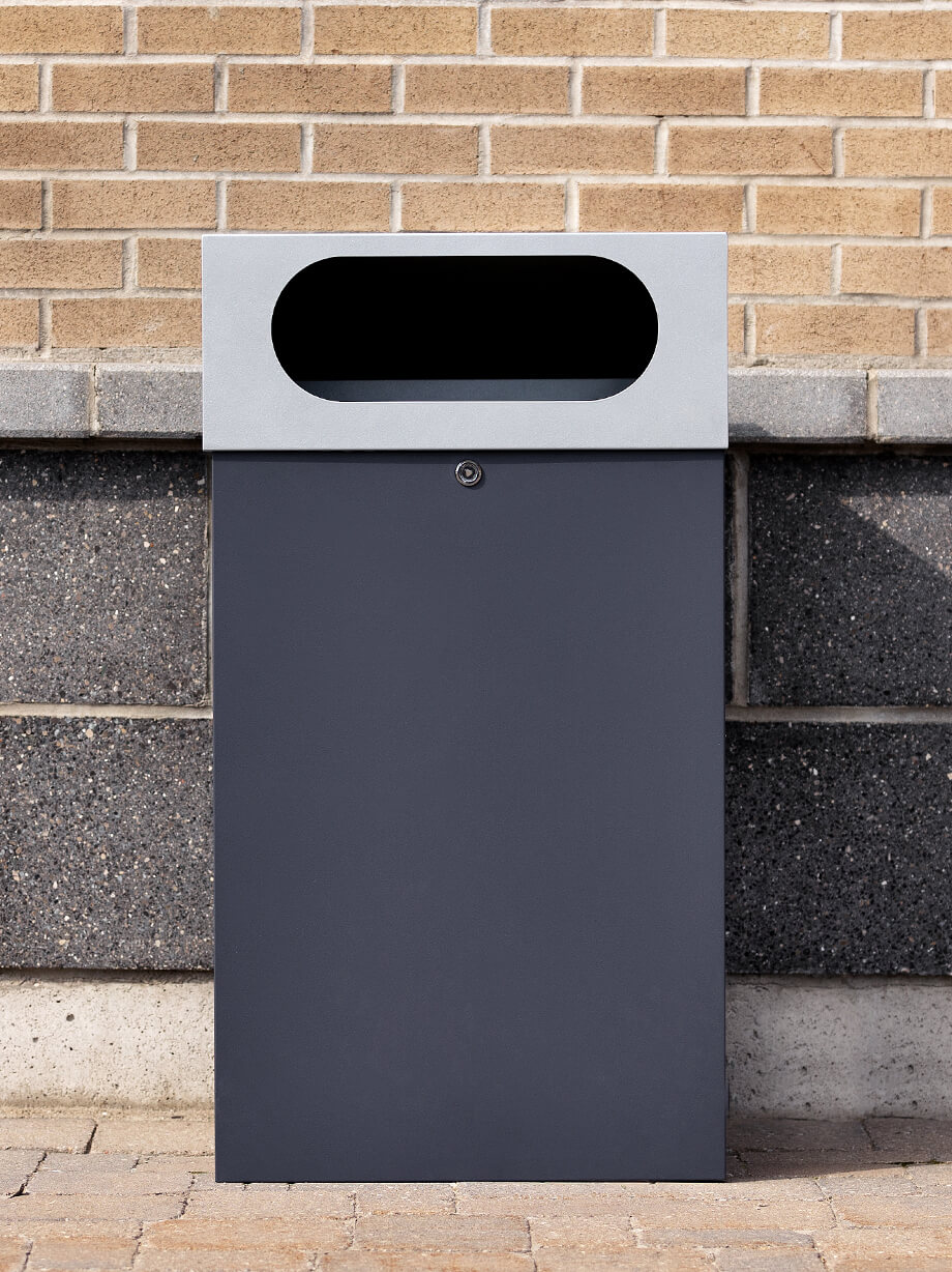 all metal powder coated outdoor waste or recycling bin with sloped hinged lid and large oval opening sitting outside a highschool