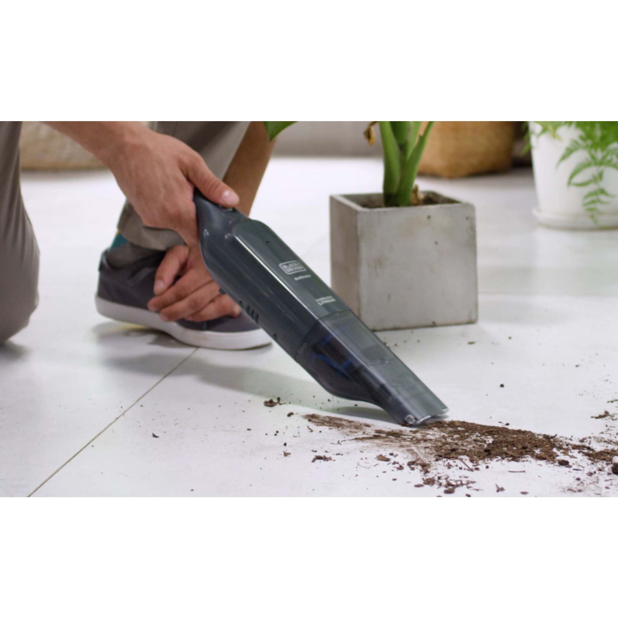 Person cleaning dirt off the tile floor near a freshly potted plant