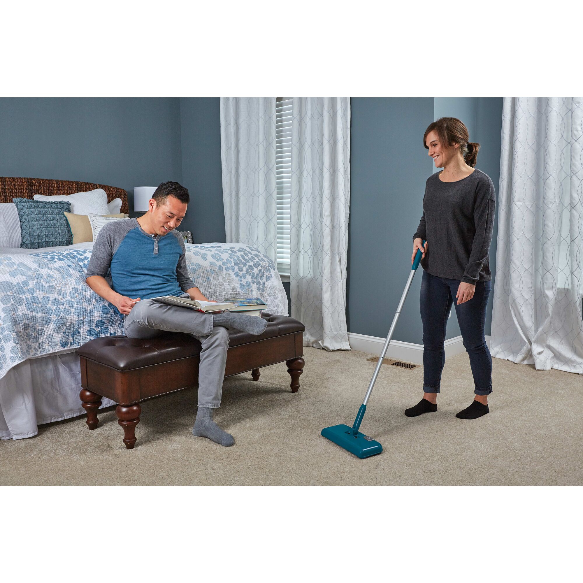 Powered Floor Sweeper being used by person to clean bedroom carpet.