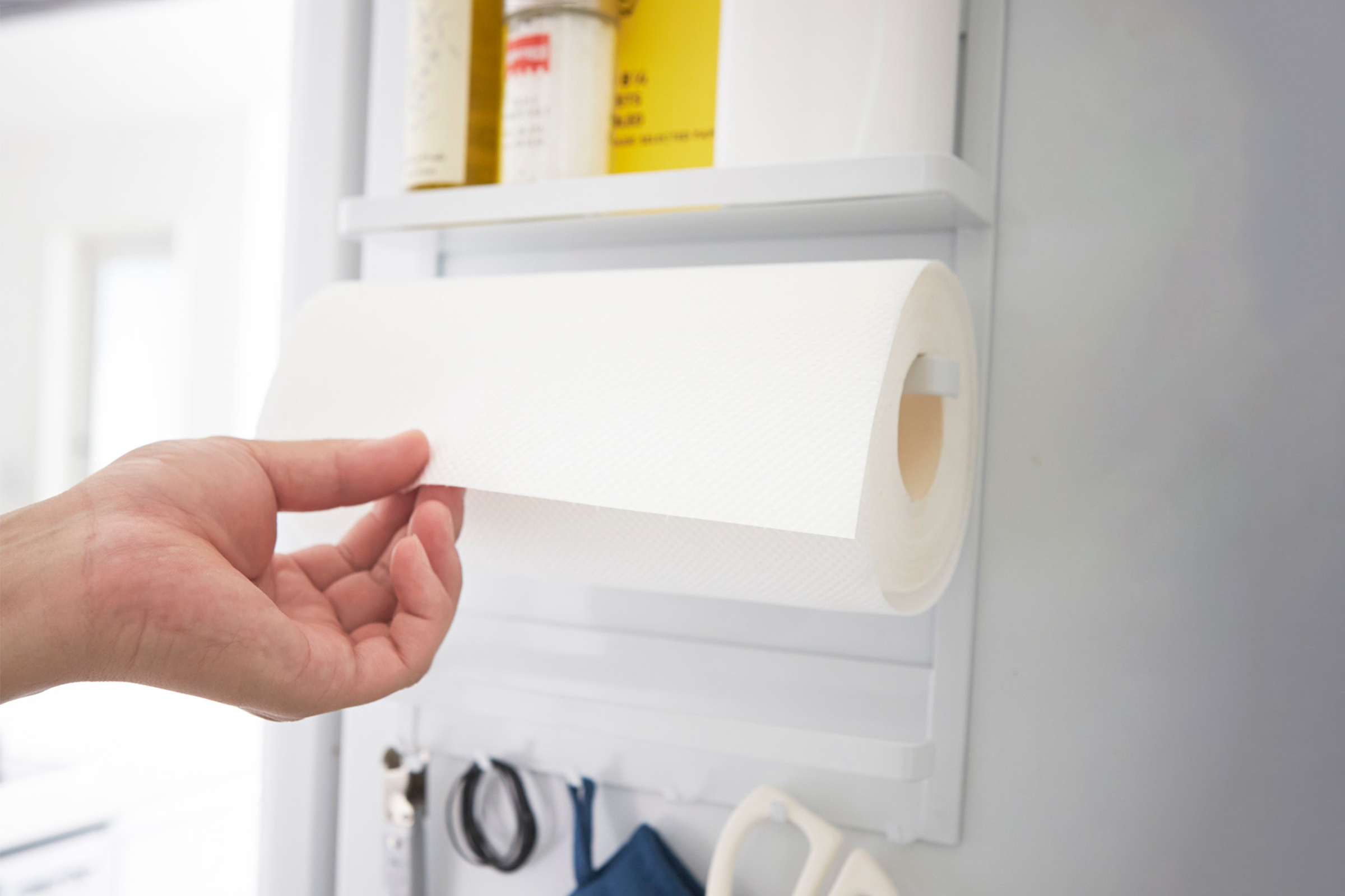 Front view of hand grabbing paper towel from white Magnetic Organizer by Yamazaki Home.