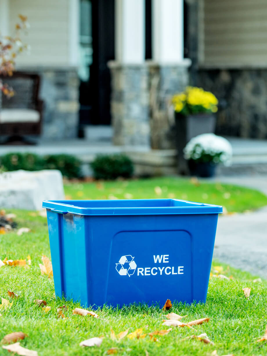 durable HDPE blue plastic recycling container with we recycled on the side sitting on a residential front lawn