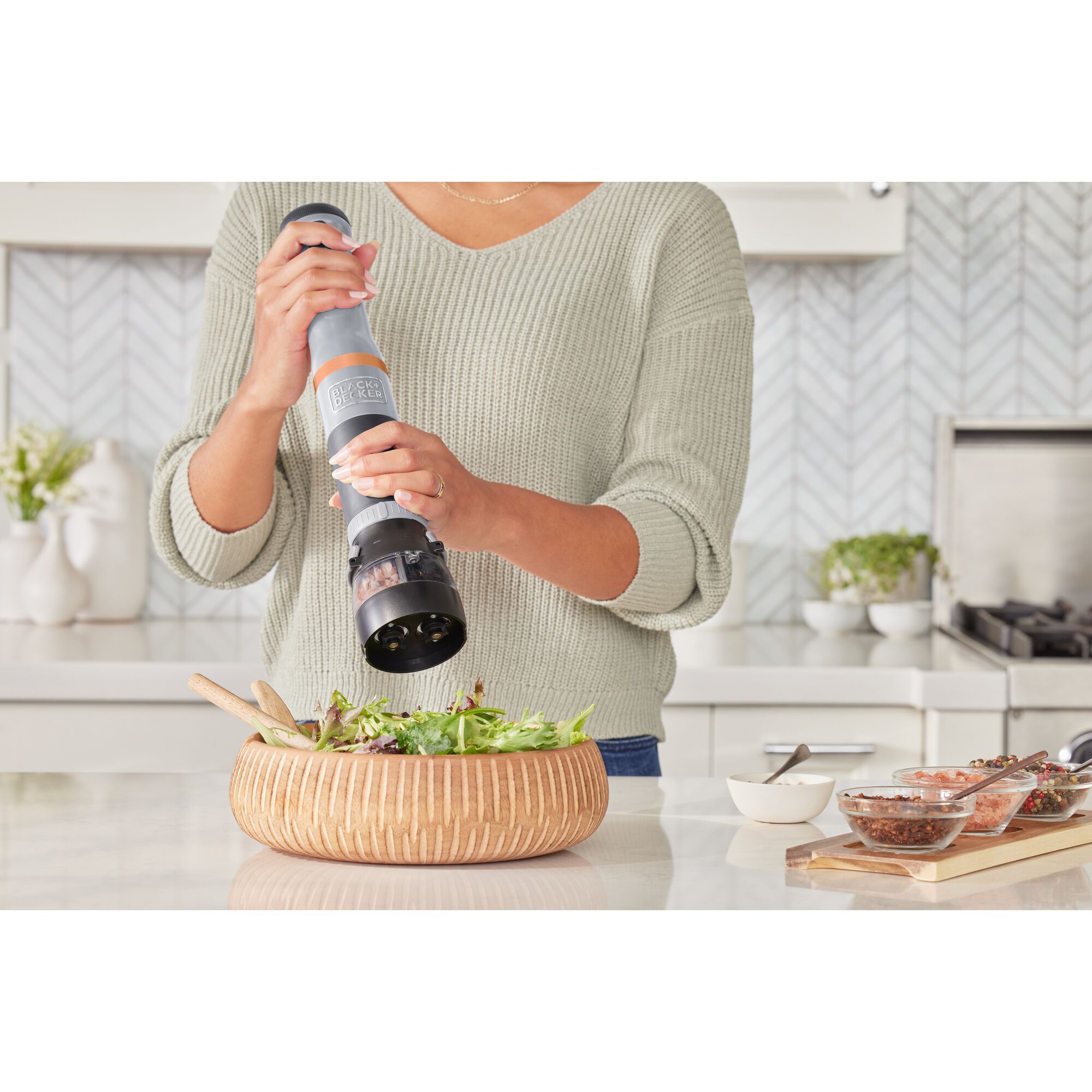 Talent using the grey BLACK+DECKER kitchen wand spice grinder attachment to add spices to a salad