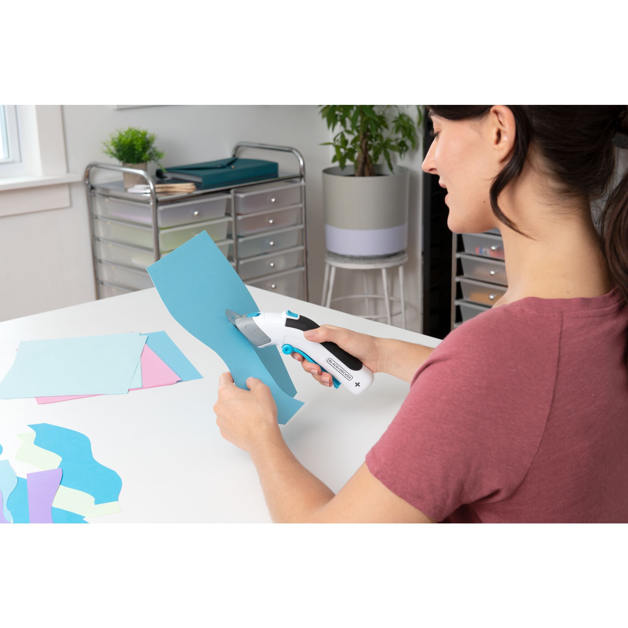 woman sitting in a craft room using BLACK+DECKER cordless power scissors to cut curved strips of colored paper