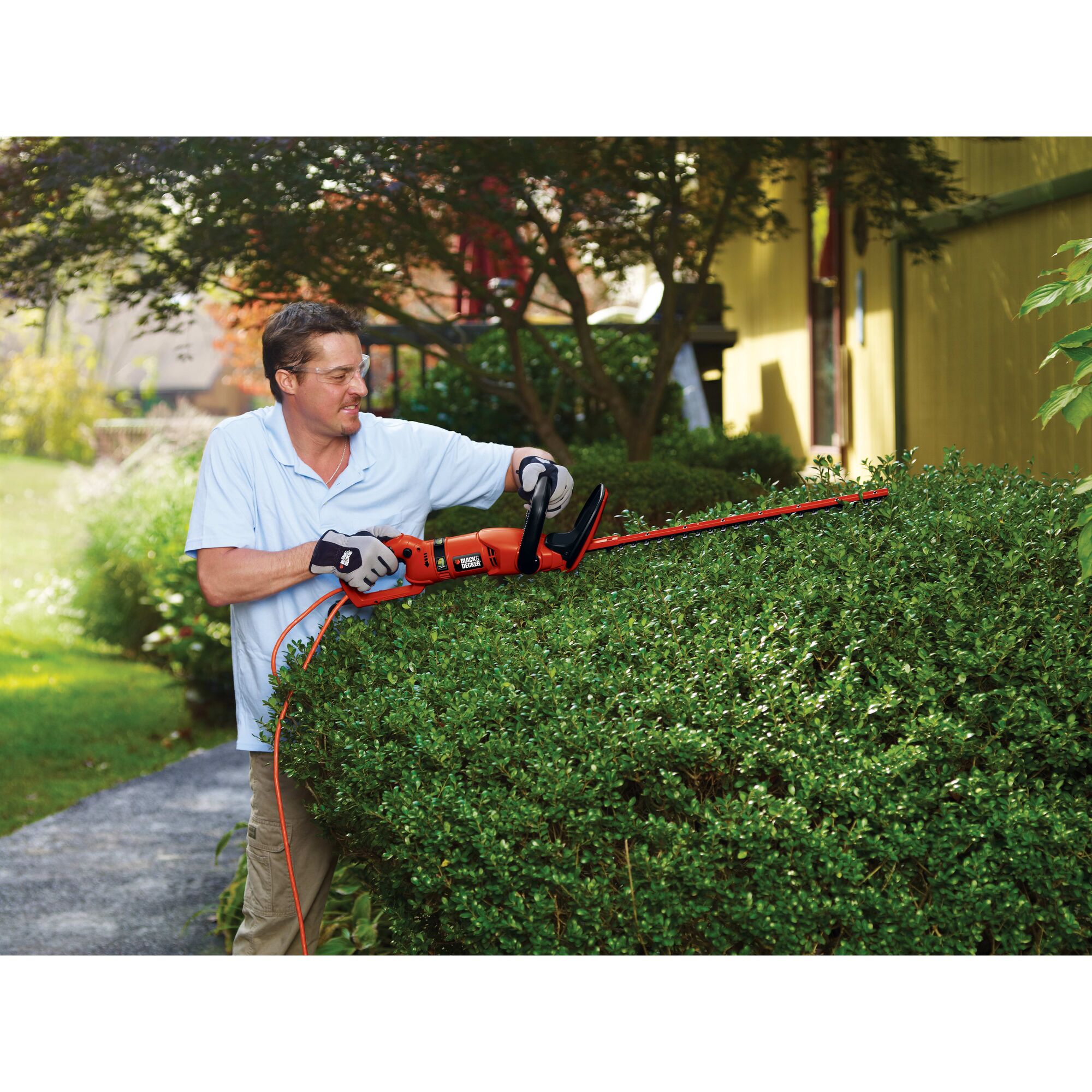 24 inch hedge trimmer with rotating handle being used by a person to trim hedge.