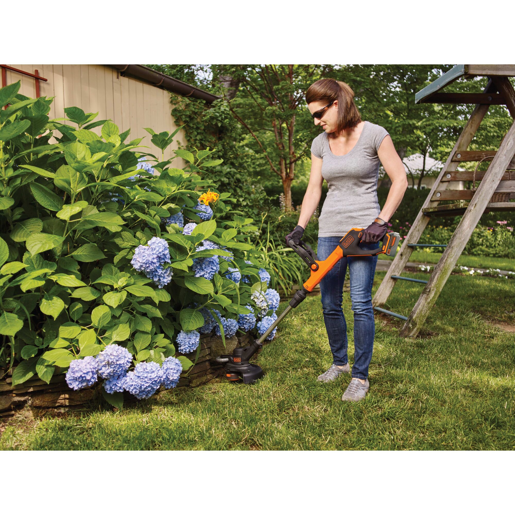 Woman using 20V Max Lithium Easyfeed string Trimmer/Edger near a garden and playset.