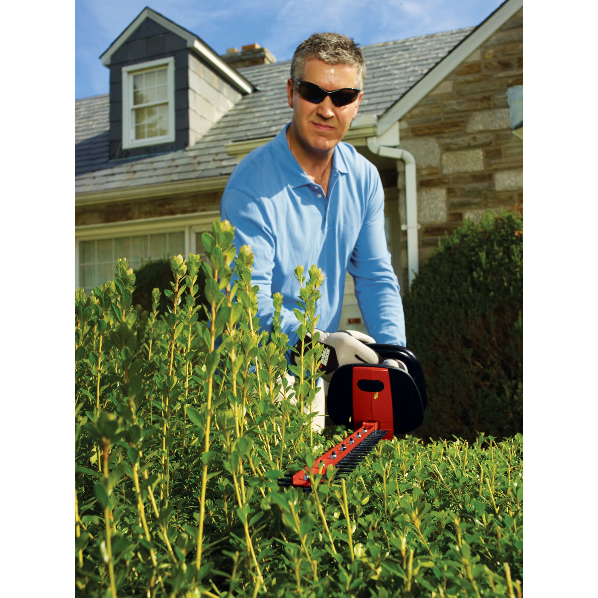 24 inch hedge trimmer with rotating handle being used by a person to trim a bush.