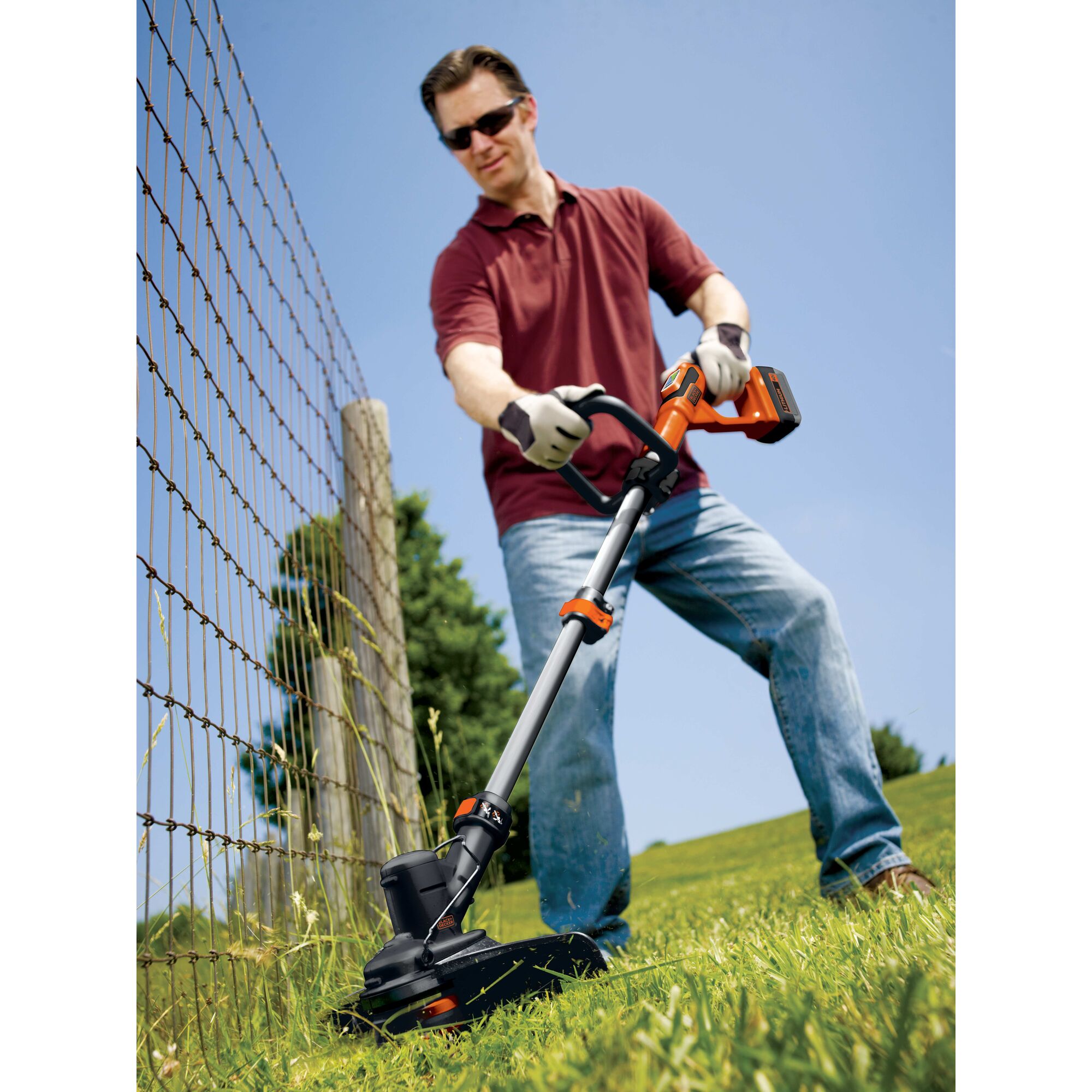 Man using 40 Volt Max String Trimmer to trim grass near a fence.