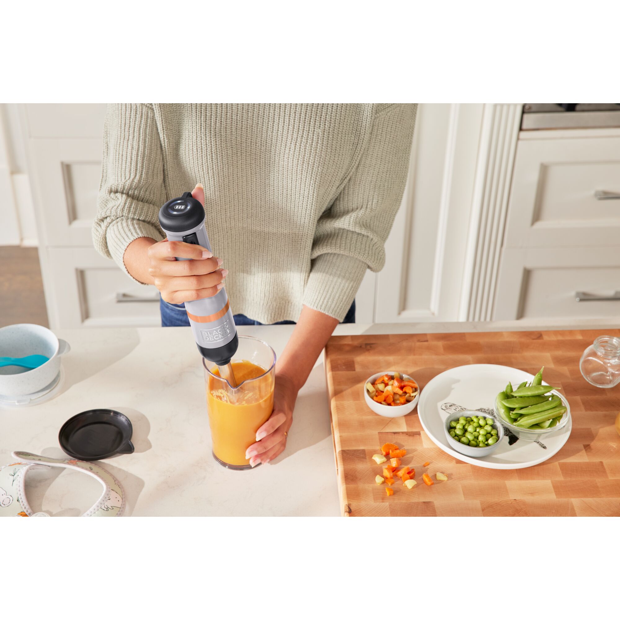 Talent using the grey, BLACK+DECKER kitchen wand immersion blender to prepare baby food