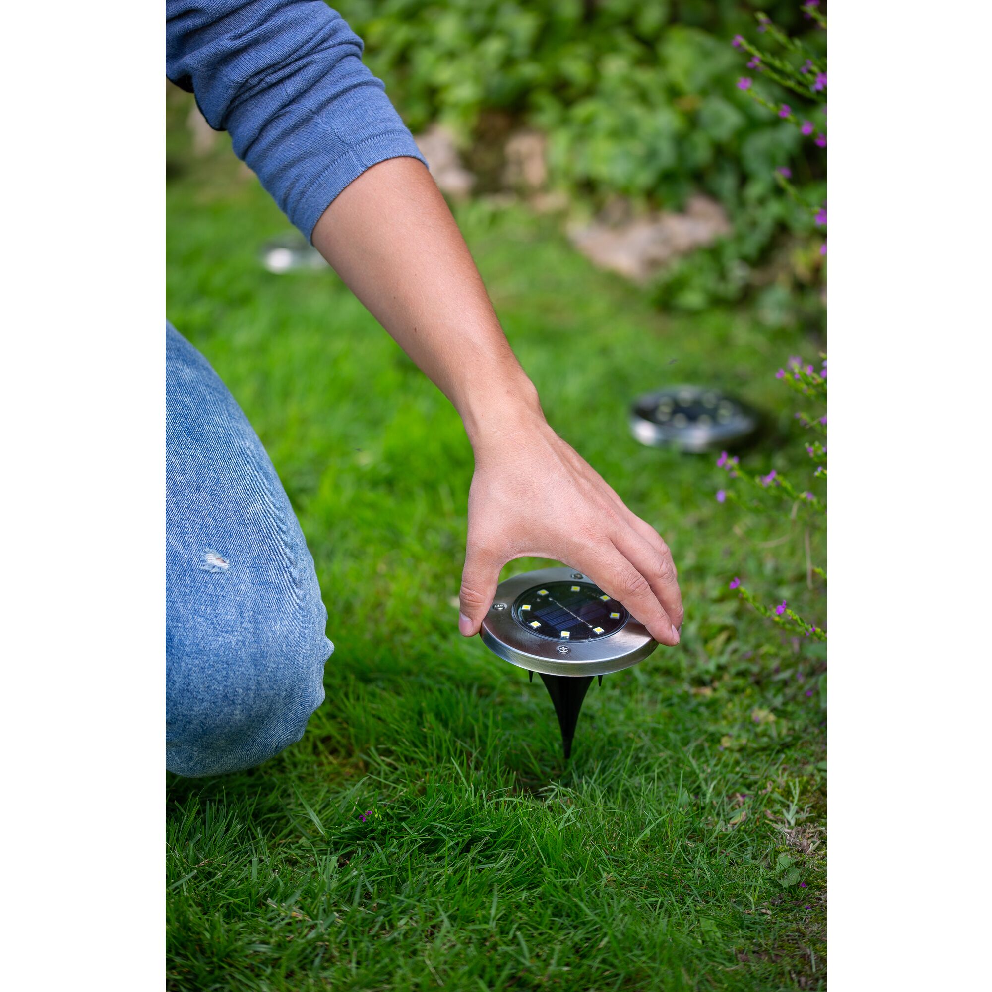 Hand pushing the BLACK+DECKER Solar Disk Light into the ground.