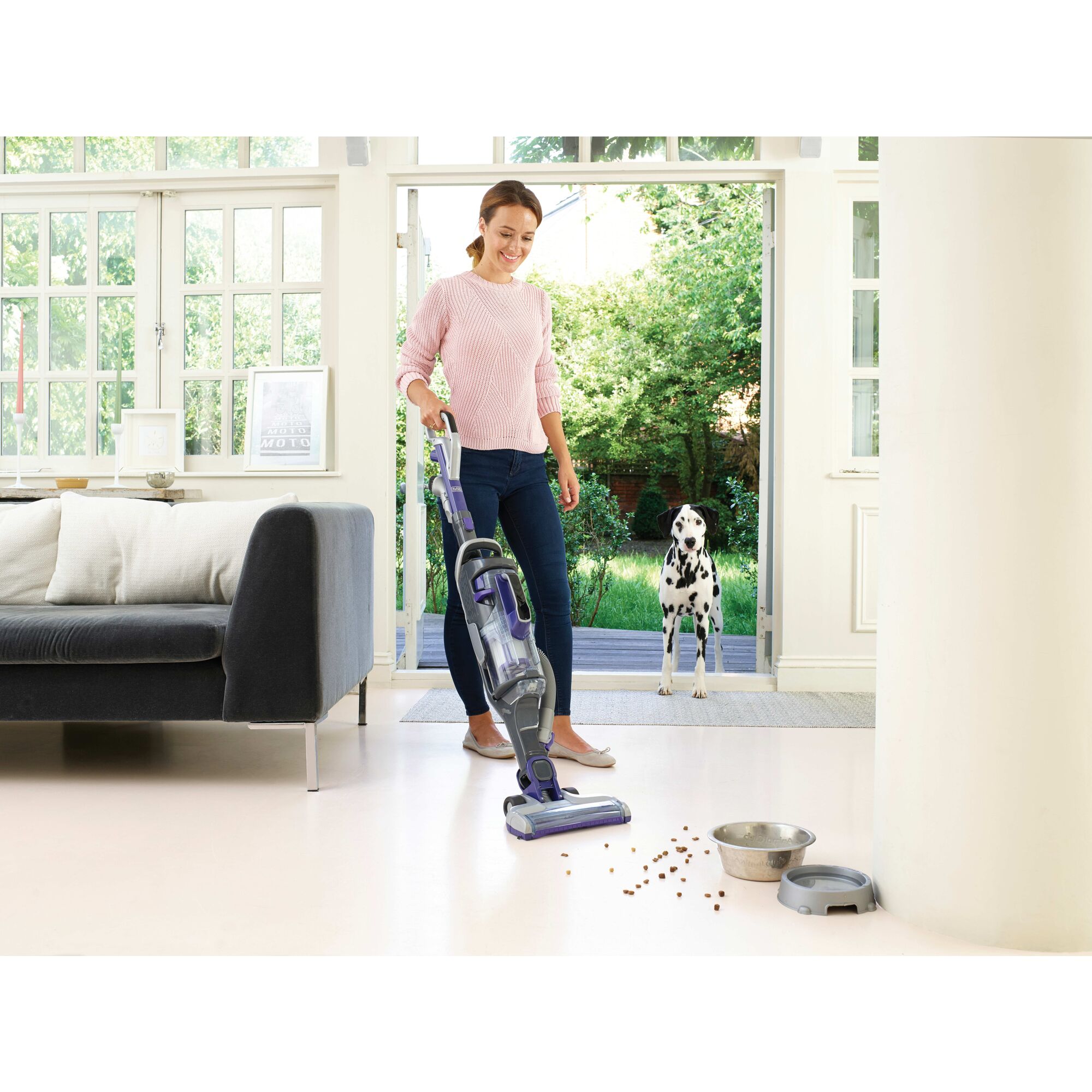 Person using BLACK+DECKER stick vacuum in living room near dog bowls