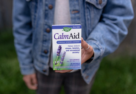 Person holding package of CalmAid in hand while standing outside.
