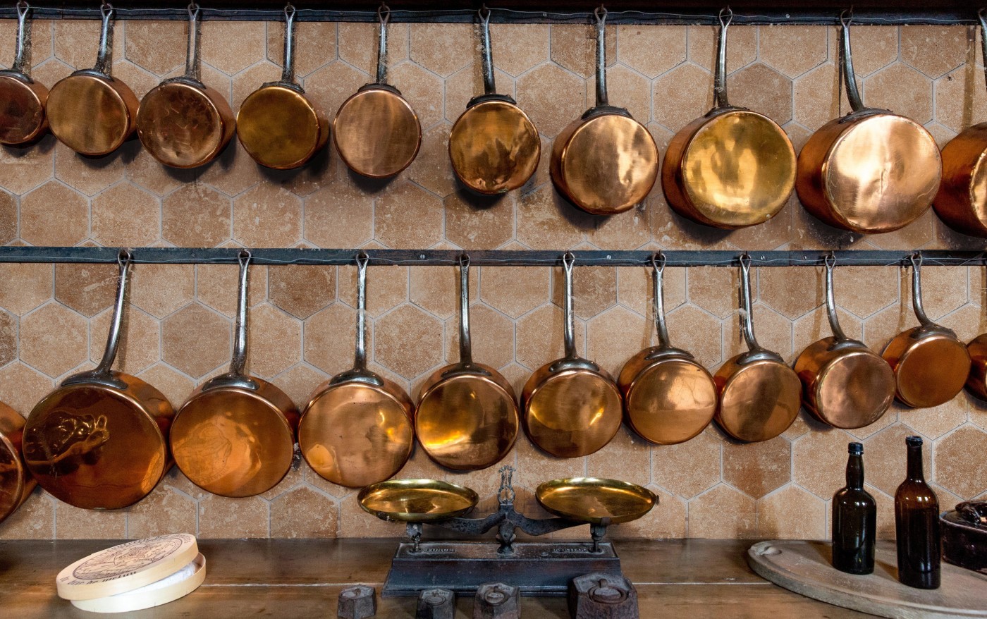 copper pots and pans hanging on a hex tile wall in a kitchen.