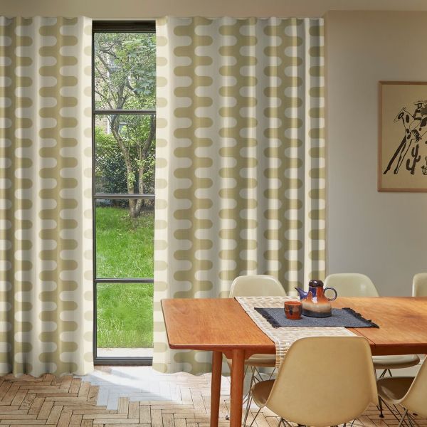 Floor-length beige-and-white patterned curtains hang on either side, parted to reveal a narrow four-pane window; dining room with wooden table and cream chairs, soft daylight and a green garden outside.