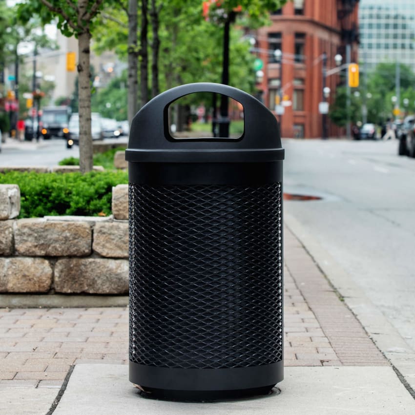 black powder coated steel waste container with a black plastic domed lid and liner on the side of a busy city street