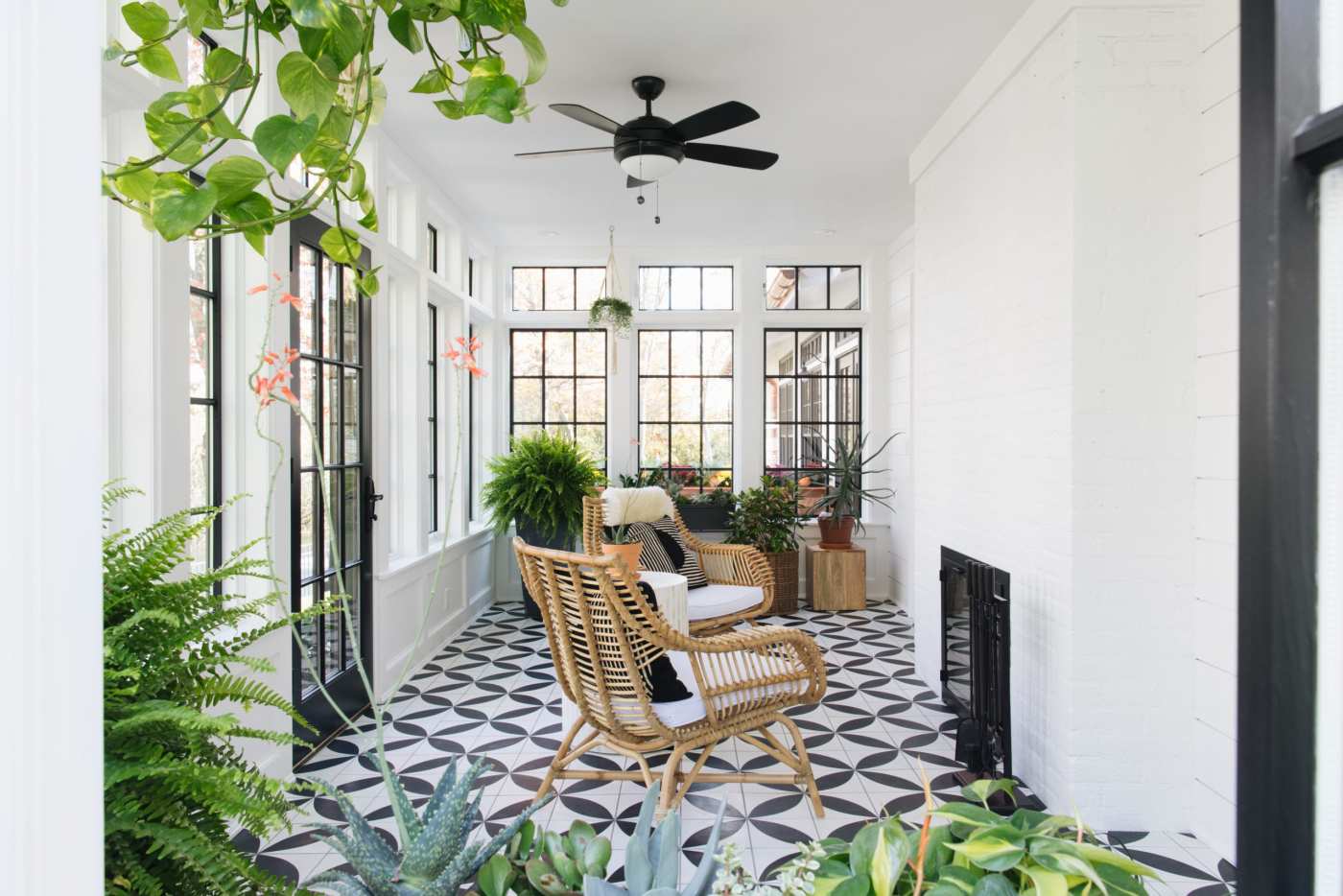 a black and white tiled porch with a wicker chair and plants.