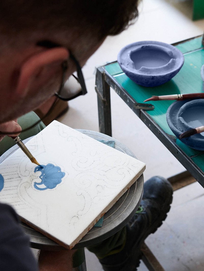 a man is painting a blue design on a white tile.