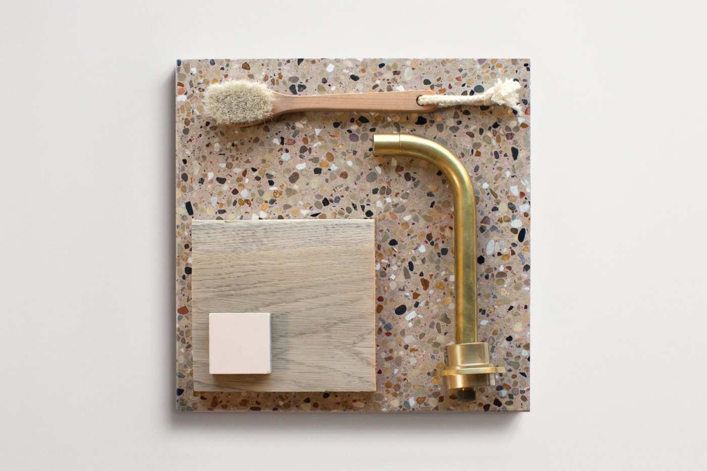 a square tile with a terrazzo pattern with a brush, a gold faucet, and other items on it.